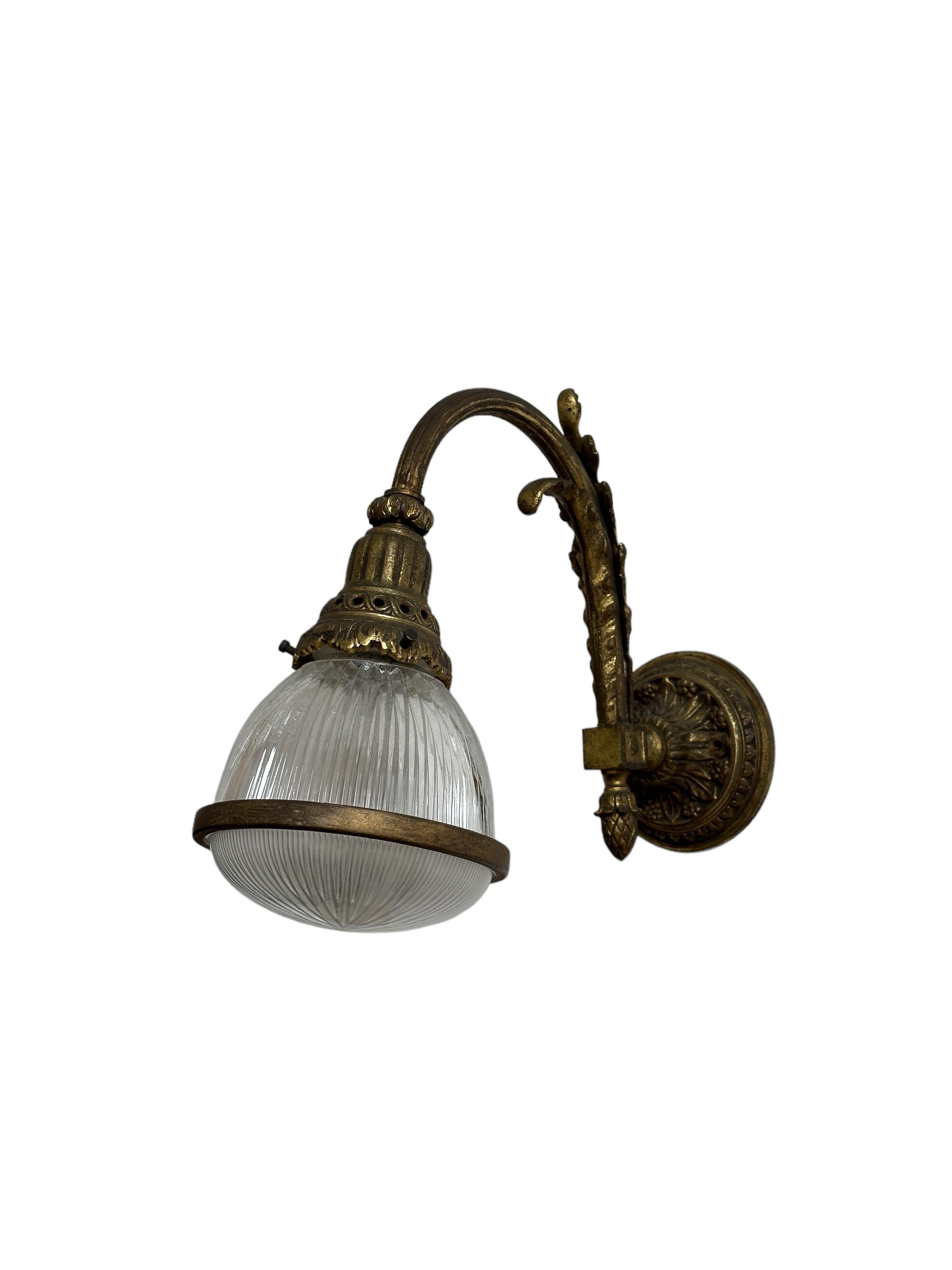 - An extremely rare pair of gilt bronze Holophane wall lights, France circa 1920.
- Decorative backplate and swan-like gallery in gilt bronze, which houses the upper prismatic Holophane shade.  The often absent lower dish held together with an