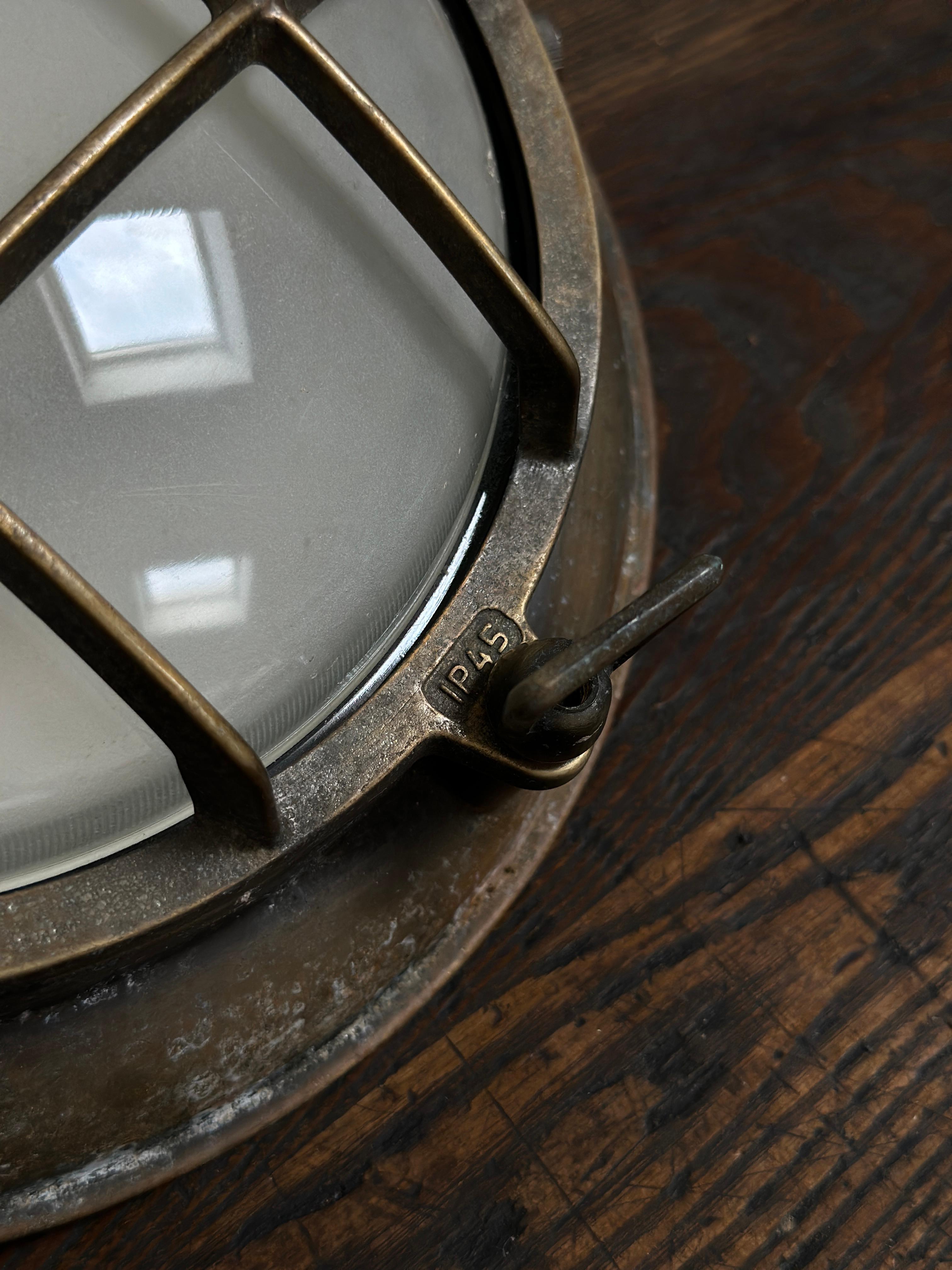 - A pair of brass circular ex-military wall lights with obscure convex glass shades, English circa 1930.
- Wonderful detail across the heavy brass rims each of which are stamped 'P45', the upper cross section unscrews to access the glass and bulb