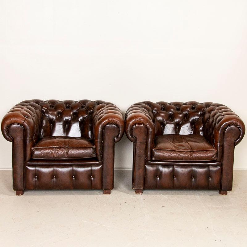 This handsome pair of Chesterfield club chairs are inviting with their deep seats, rolled arms and Classic tufted backs. The vintage brown leather shows signs of typical wear commensurate with age including some scuffs, scratches, crackles and one