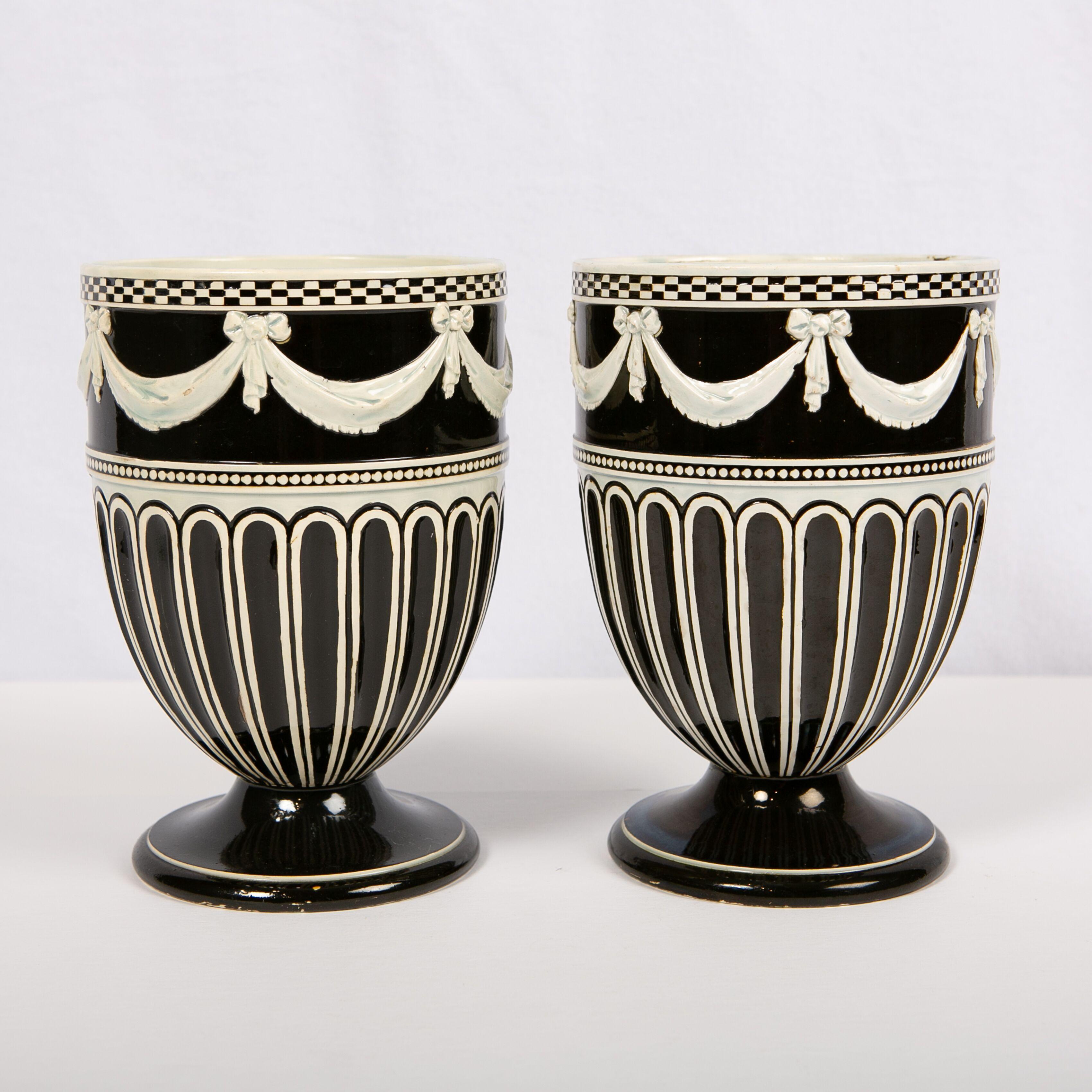This pair of late 18th century Wedgwood pearl-glazed creamware vases is a powerful and beautiful example of Wedgwood's skill and artistry. The vases feature three types of workmanship. Around the top edge, we see engine-turned, checkerboard