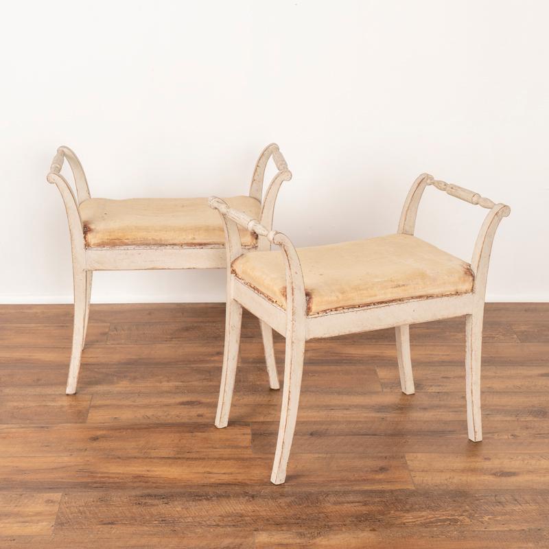 This lovely pair of Swedish stools or tabourets have graceful curved, splayed legs which add an elegant touch to the pair. The turned hand rests provide stability as well as balanced beauty. The aged patina of the later paint adds to their charm.