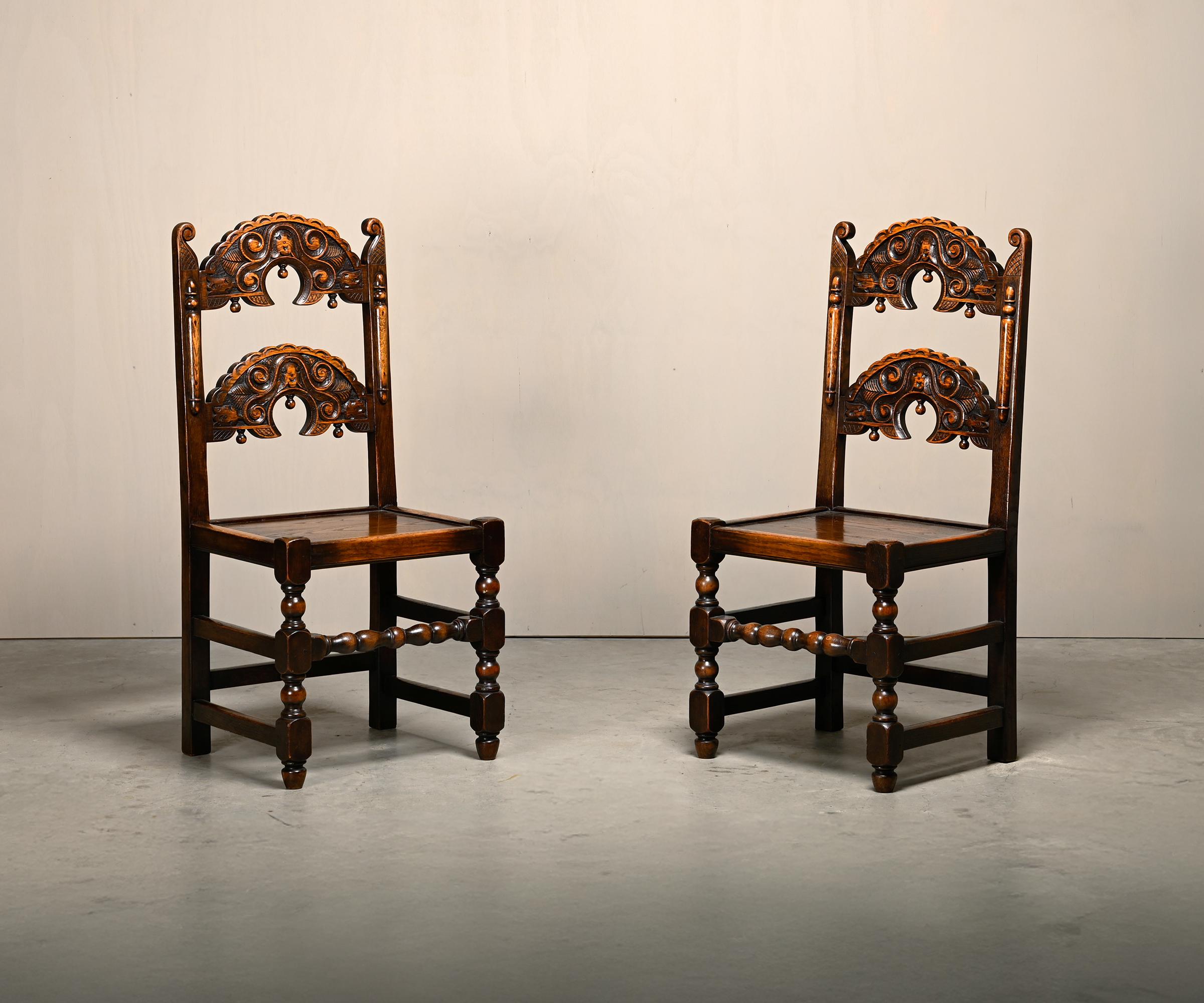 Antique pair of Yorkshire Back Stools / Side Chairs, England, 18th century. Solid oak with two curved backrests featuring hand-carved natural motifs. The stained oak is beautifully aged and the chairs are very solid.

Documented in Tobias Jellinek’s