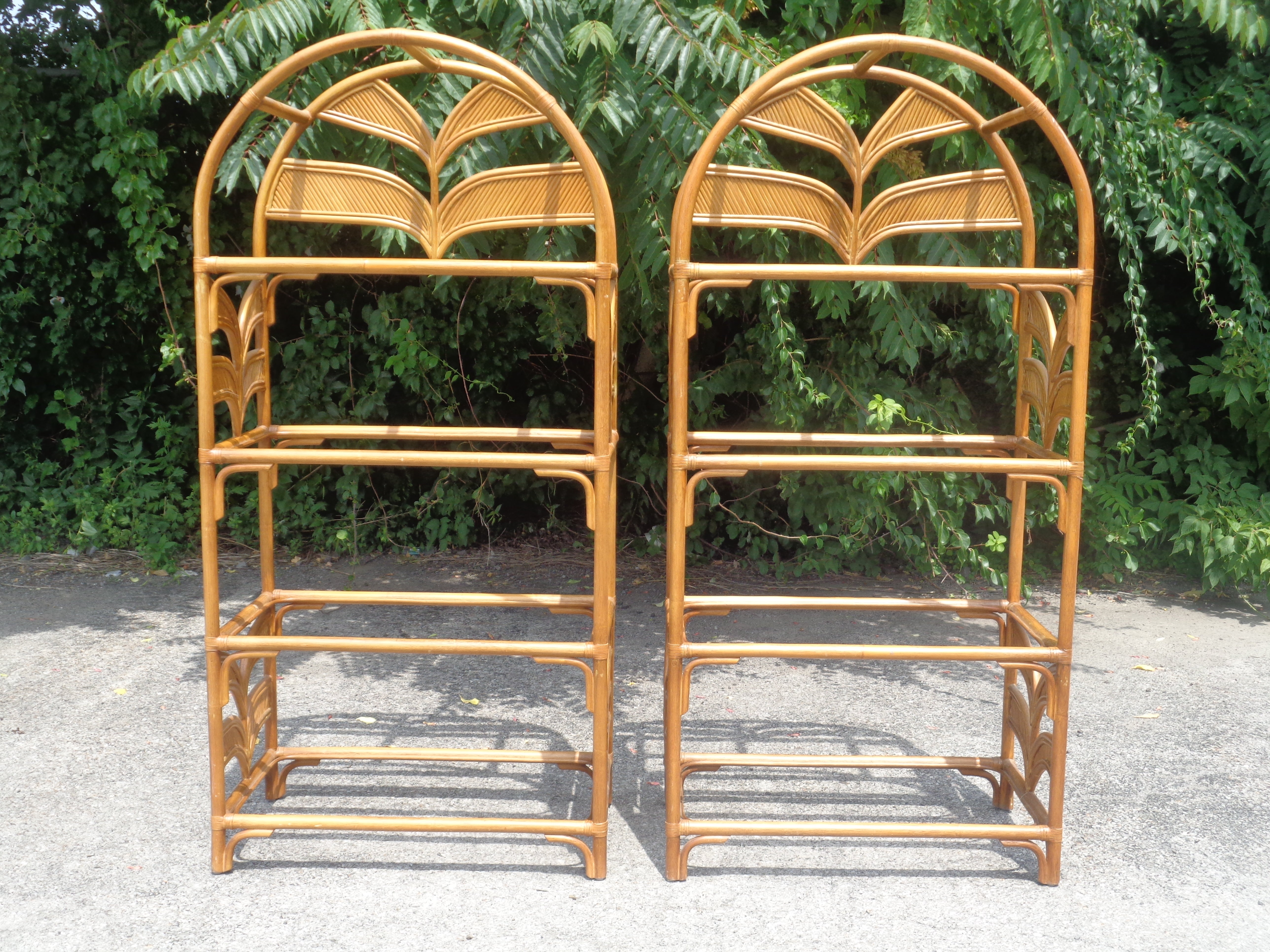 A great looking matched pair of leather wrapped rattan arch top etageres / free standing shelving units w/ a pencil reed like palm leaf decoration at top and sides. Overall beautiful original rich honey colored surface. Each etagere w/ four fixed