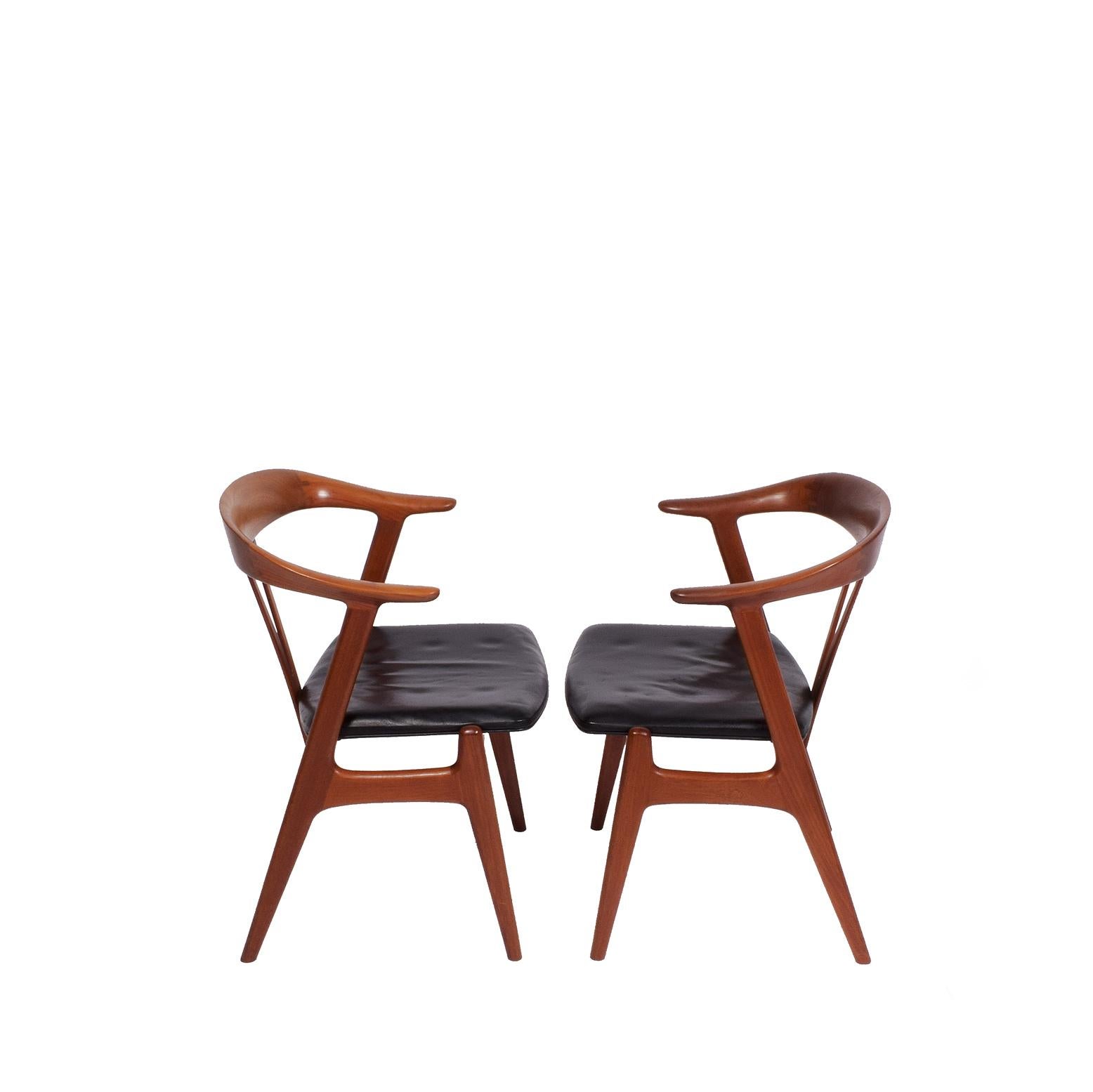Solid teak armchairs with nice carpenter detail on the backs of the chairs, original black leather and condition.