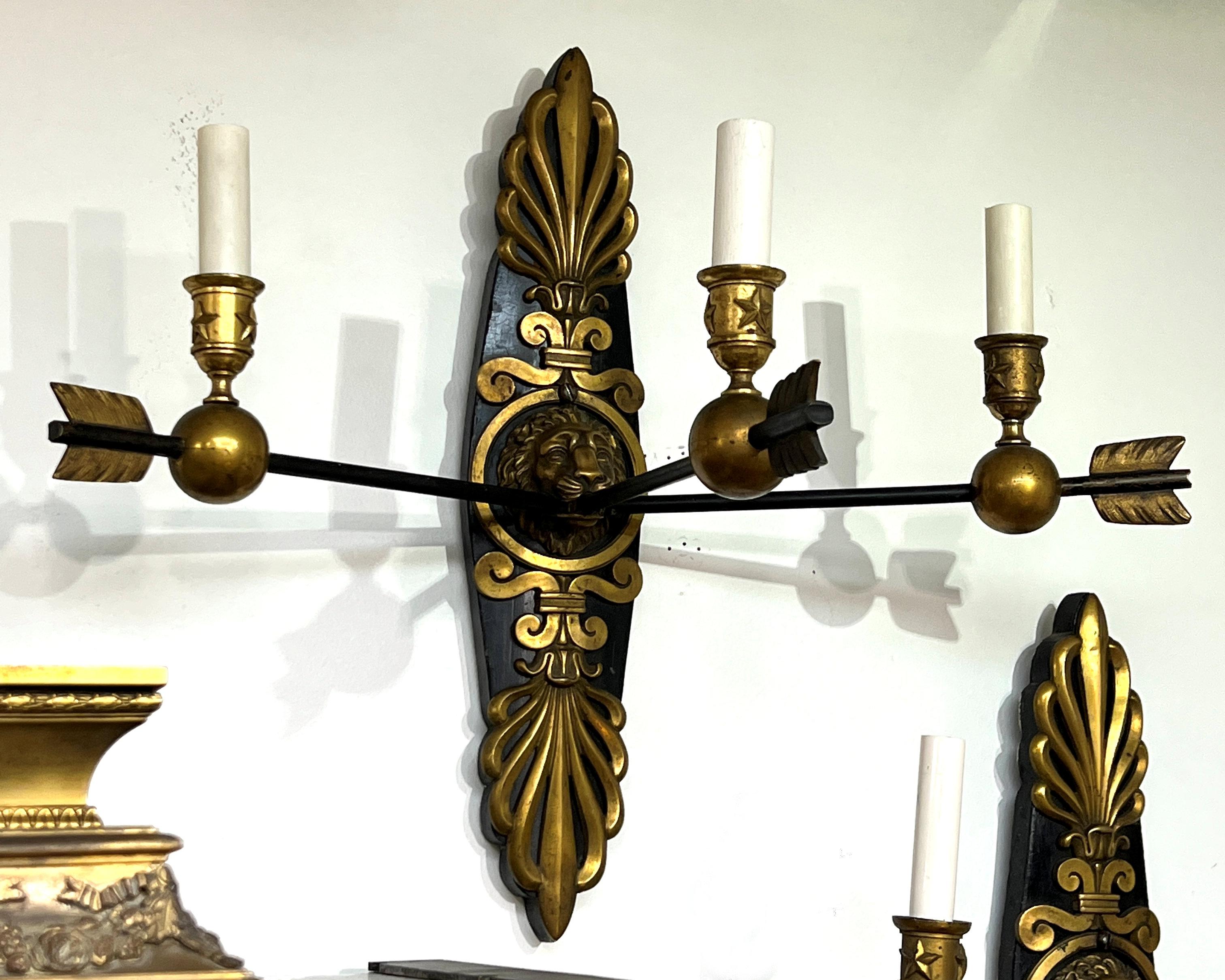 Our French Empire style sconces have three arrow-form candle arms ending with candleholders with star motifs, and emanate from lion mask back plates with palmette crests that are mounted on ebonized wooden back plates. Standard size sockets with