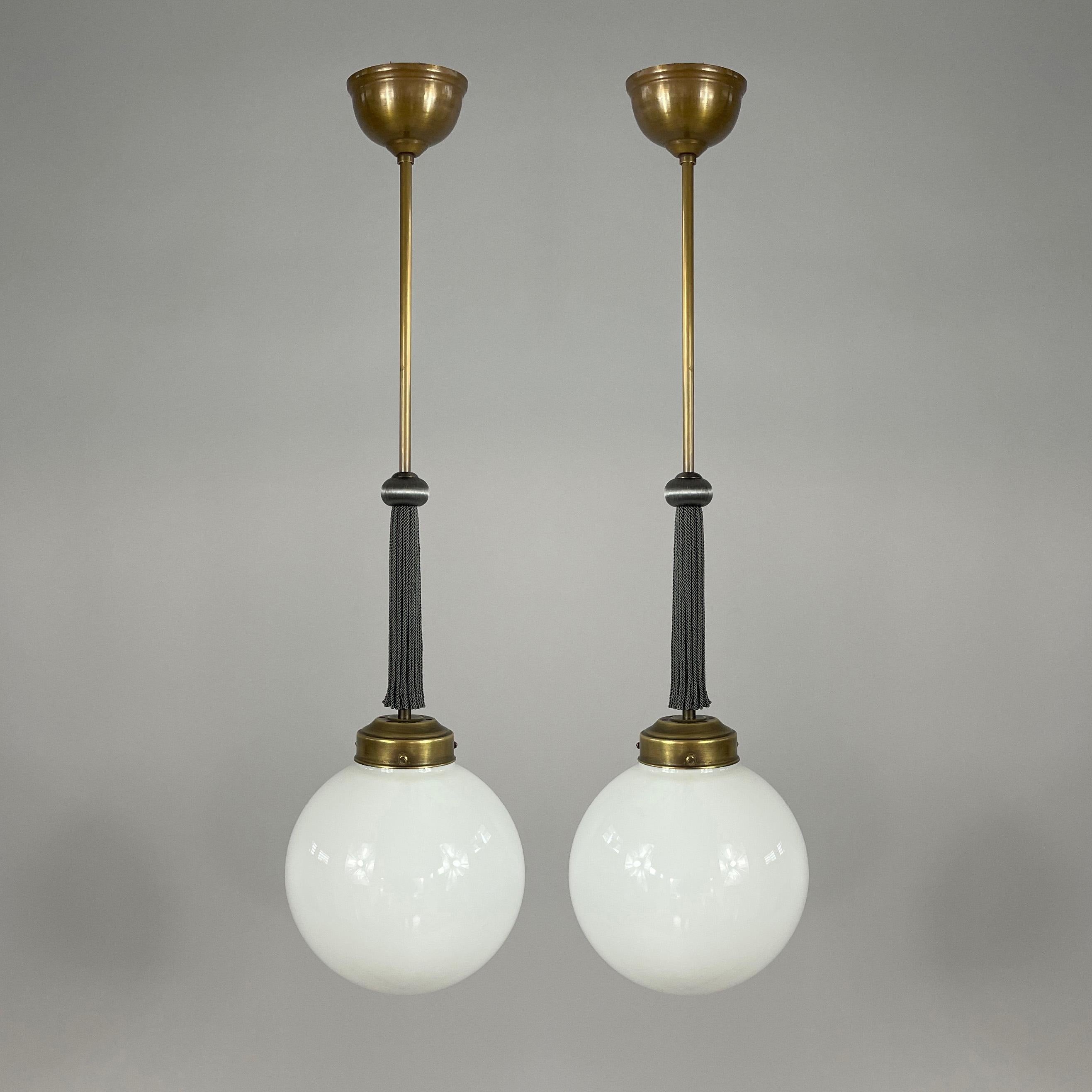 German Art Deco Opaline Pendants, 1930s, Bauhaus era

The lights feature elegant German Art Deco design with a patinated brass rod and canopy, complemented by a decorative dark grey silk tassel. The spherical opaline glass shades emit a soft,