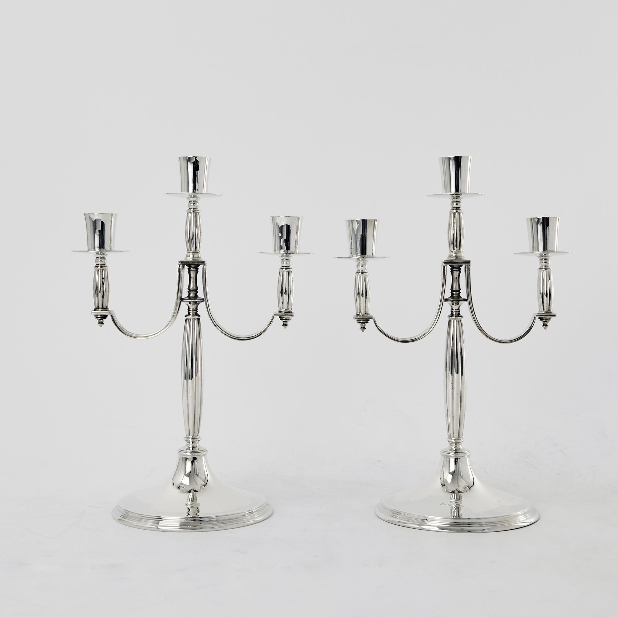 A pair of unusual and wonderful quality three-light sterling silver candelabra in the Art Deco style with round bases supporting fluted stems with similarly fluted flat arms. These heavy quality candlesticks are made in cast sections and are not