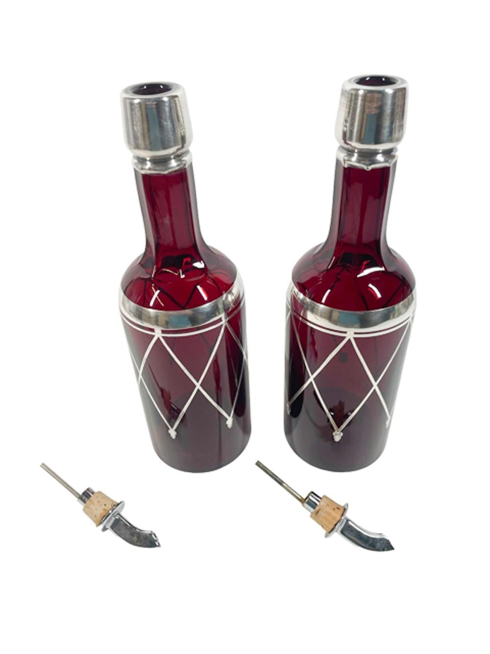 Pair of Art Deco back bar bottles or decanters in silver overlaid ruby red glass with panel faceted necks. Silvered on the collar and with bands below the shoulder with crisscrossed lines terminating with trefoil pendants. Fitted with Chrome
