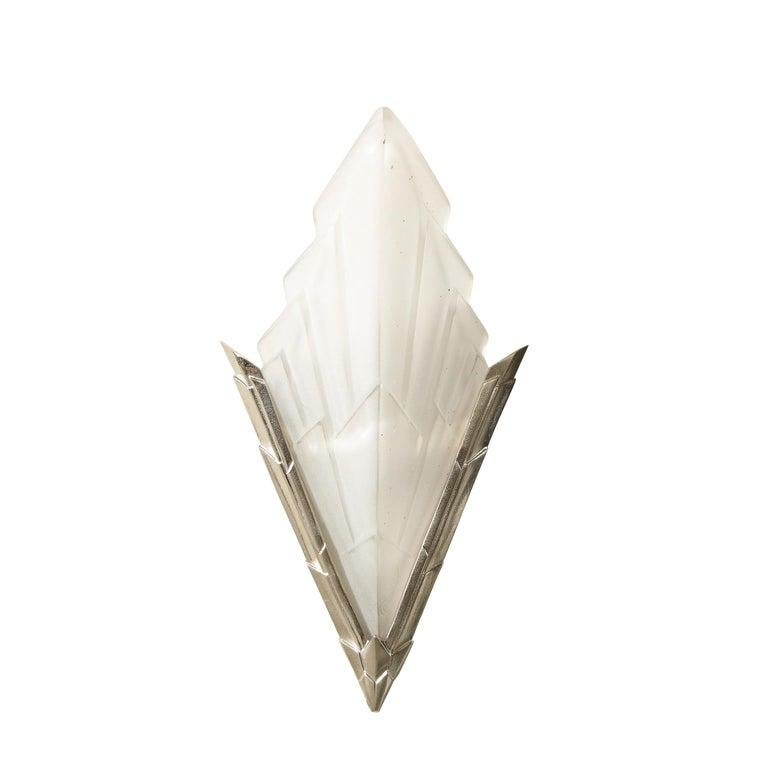 La coppia di sofisticate appliques Art Deco francesi degli anni '30 presenta due pannelli di vetro smerigliato in rilievo con un drammatico motivo a grattacielo, montati su una cornice in bronzo argentato. Le suggestive applique di forma geometrica
