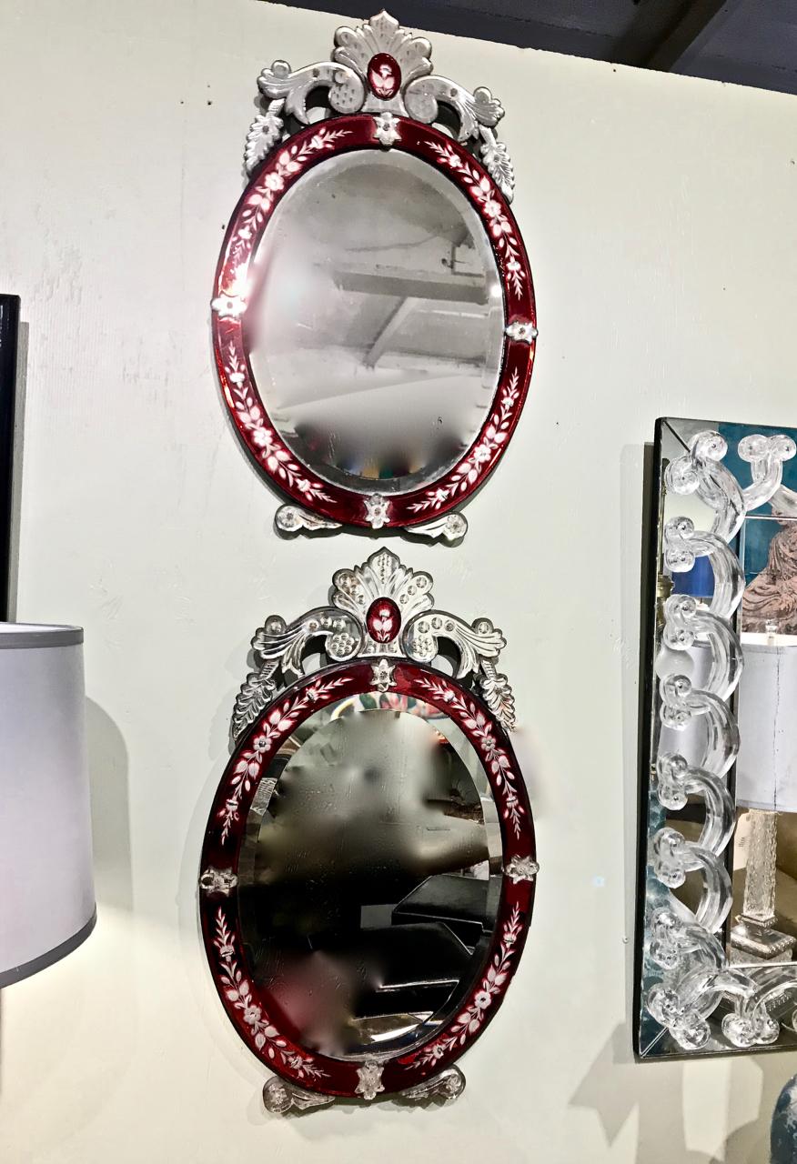 This is a wonderful pair of period Art Deco Venetian mirrors. The bevelled mirrors are framed by etched cranberry glass highlighted with mirrored glass rosettes and surmounted by a mirrored cut glass crown decoration. The mirrors are dated to the