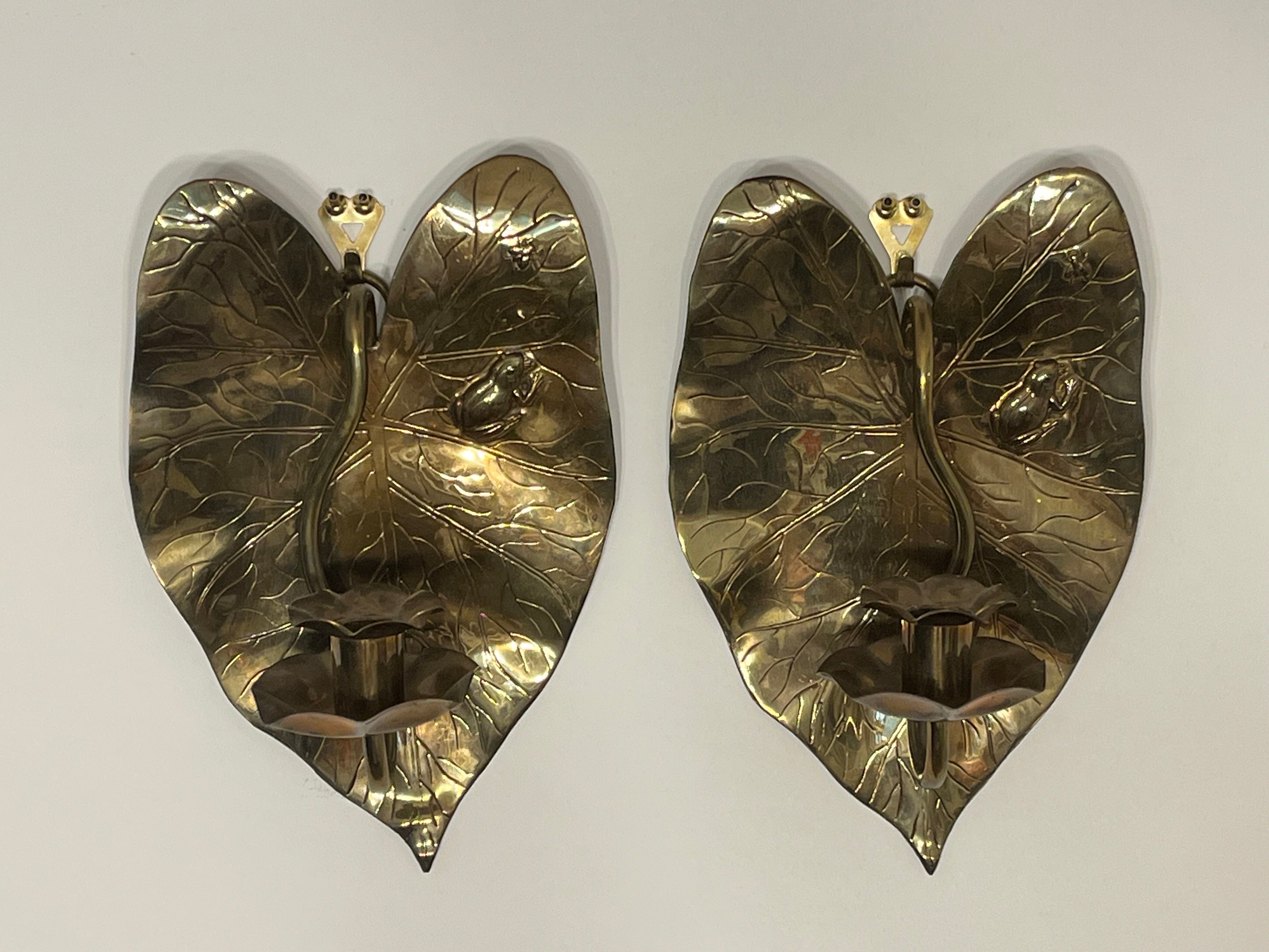 An antique, circa late 19th century, pair of English brass candle sconces. The heart shaped lily pad serves as the backplate to a wavy candle holder with a scalloped and equally wavy bobeche. The stem, as it were, slots into a cylindrical piece of