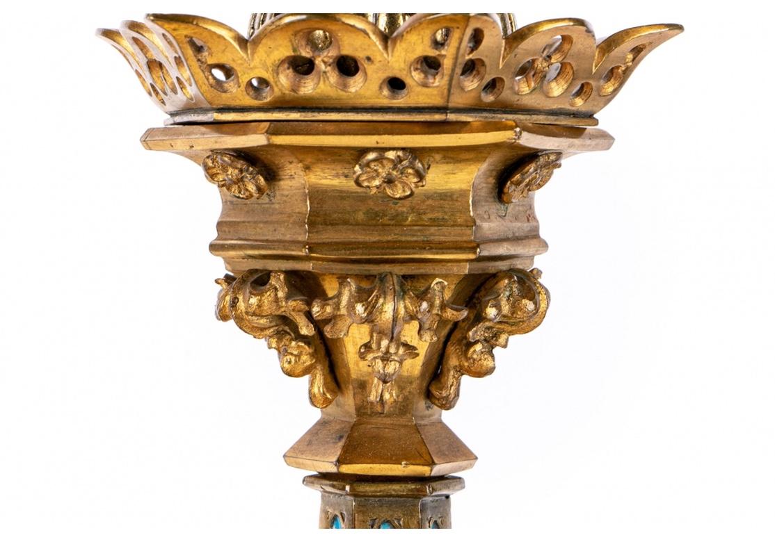 Gilt bronze and turquoise enamel. With pierced hexagonal bobeches raised on floral and scrolled standard tops. The faceted standards inlaid with turquoise enamel. Gothic style decorated arch shaped tripod legs.
H. 20 1/2