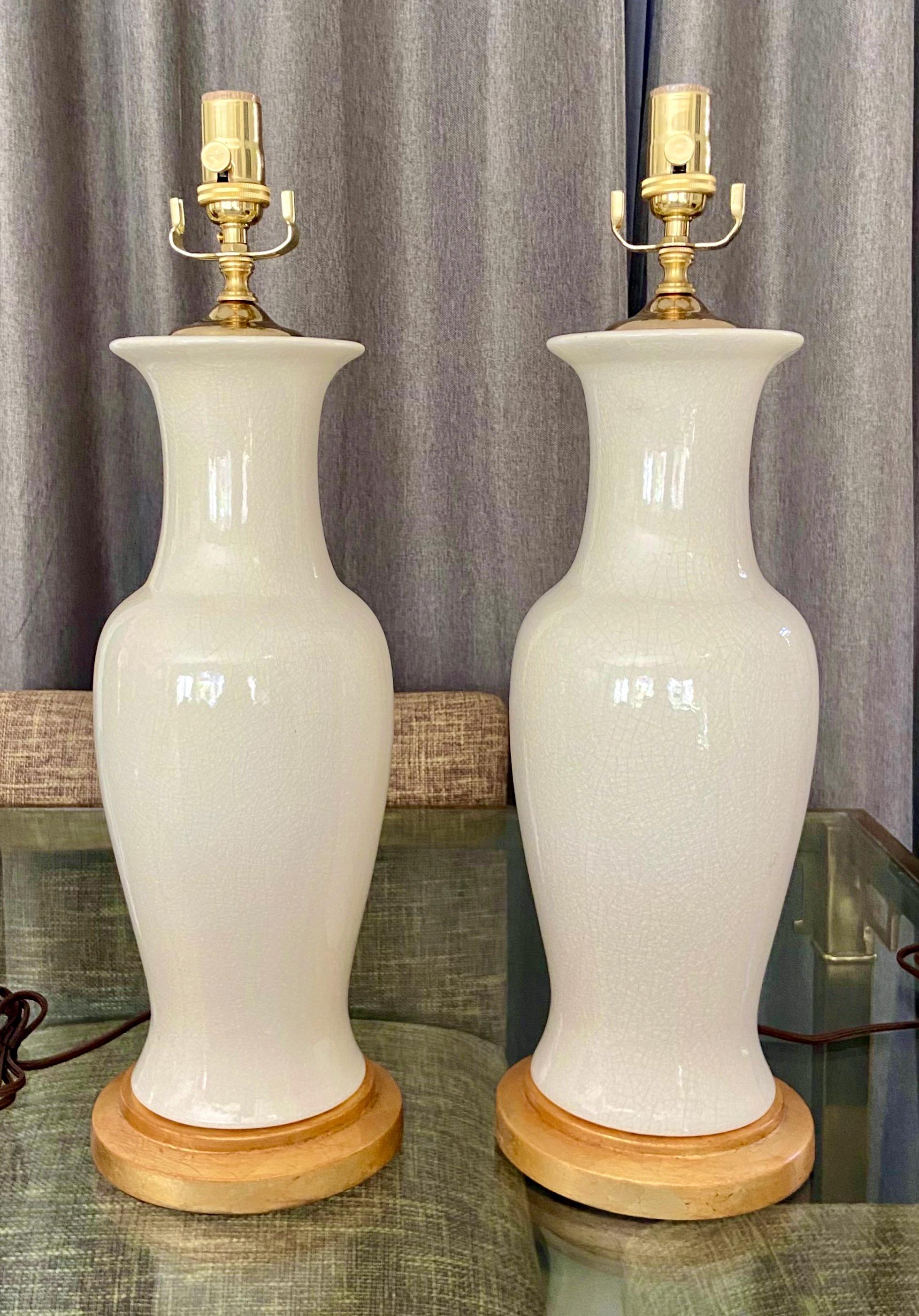 Pair of Asian white blanc de shine monochrome baluster shaped porcelain table lamps. The glazed white surface has fine crackling (craquelure) throughout. Mounted on turned giltwood bases. Newly wired with new brass 3 way sockets and cords. Overall