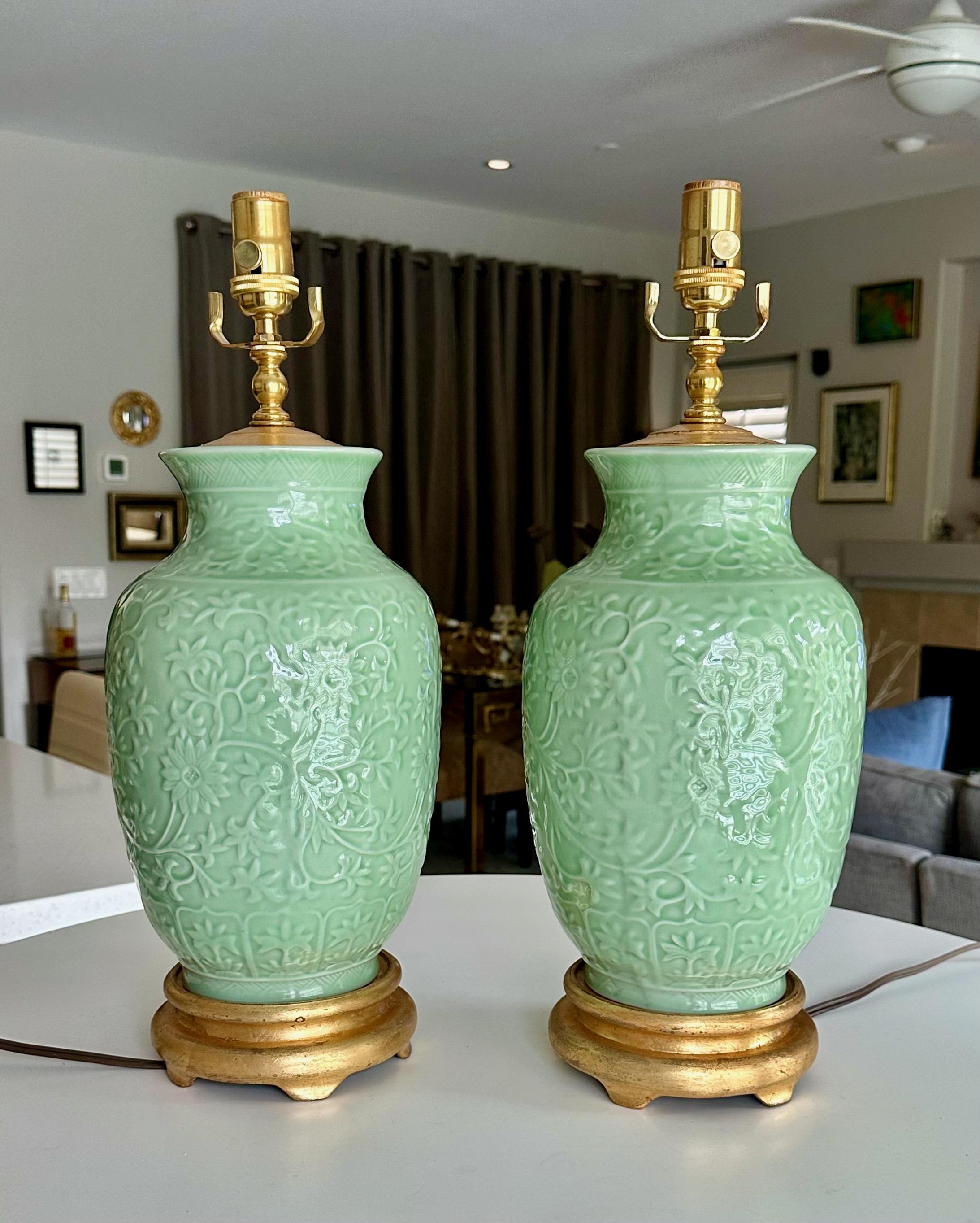Pareja de lámparas de mesa chinas de porcelana verde celadón tallada en relieve con flores y follaje. Cada una montada sobre bases de madera dorada junto con la tapa del jarrón a juego. Recién cableada con enchufes nuevos de latón de 3 vías y cables