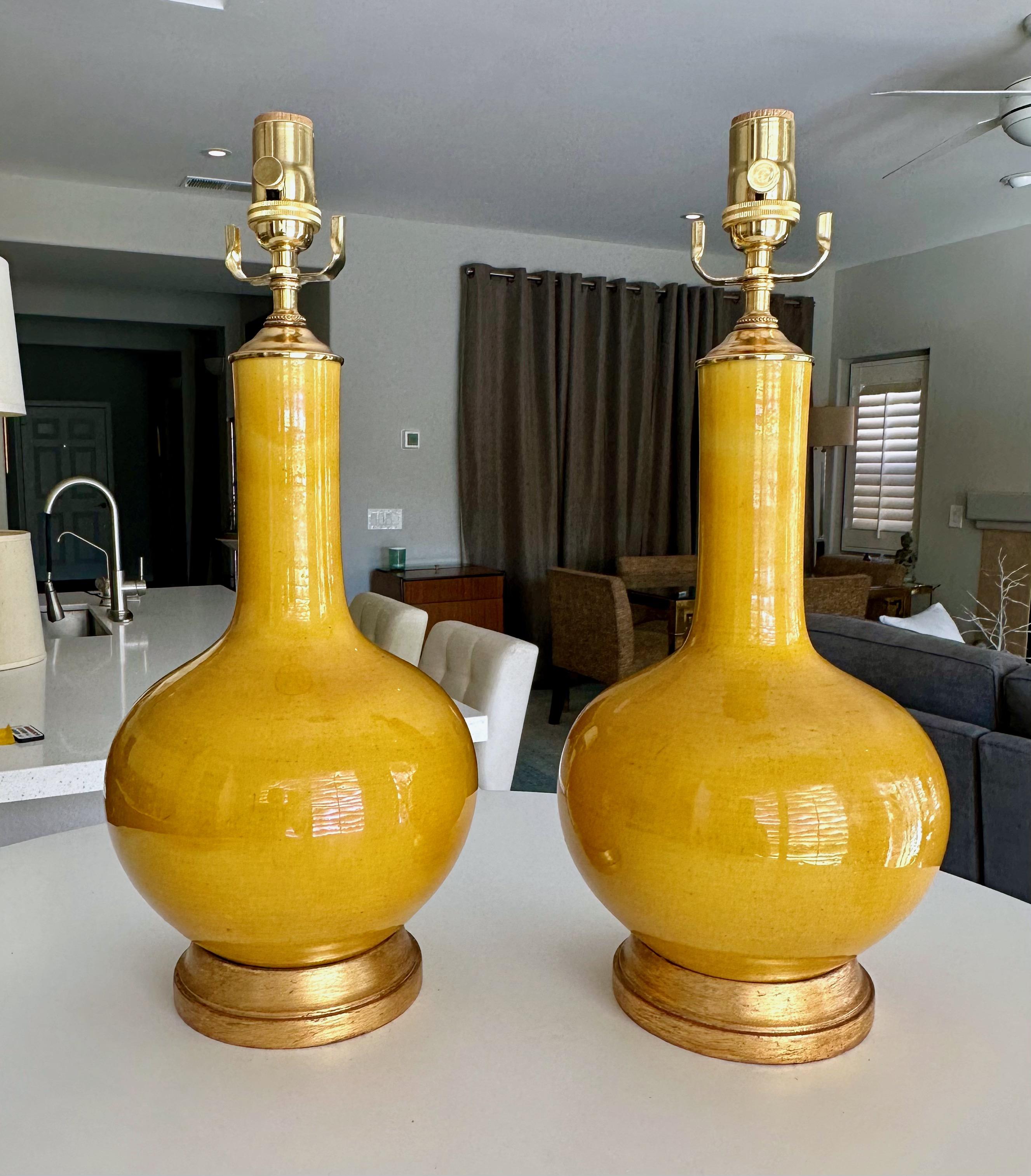 Pair of Asian style bright yellow glaze porcelain table lamps. Each mounted on gilt turned wood lamp bases. Newly wired with brass 3 way sockets. Porcelain vase portion is 13.5