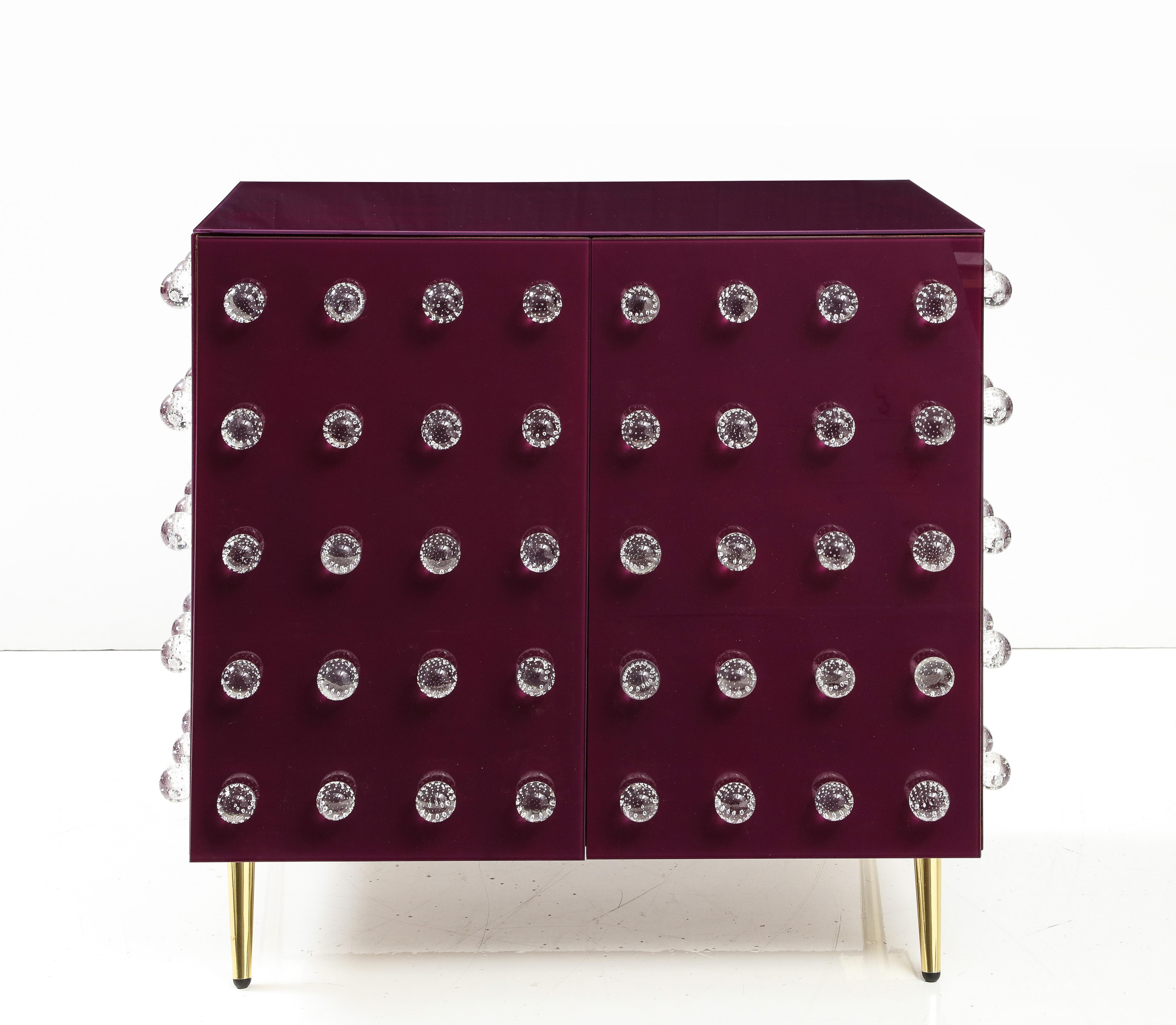 Bespoke, One-of-a-kind Pair of Aubergine Plum Glass with Murano Spheres Cabinets with Brass Legs handmade in Italy, 2023. Wooden frame is veneered or clad in reverse-painted art glass panels in a rich aubergine or plum color.  Hand-casted, solid