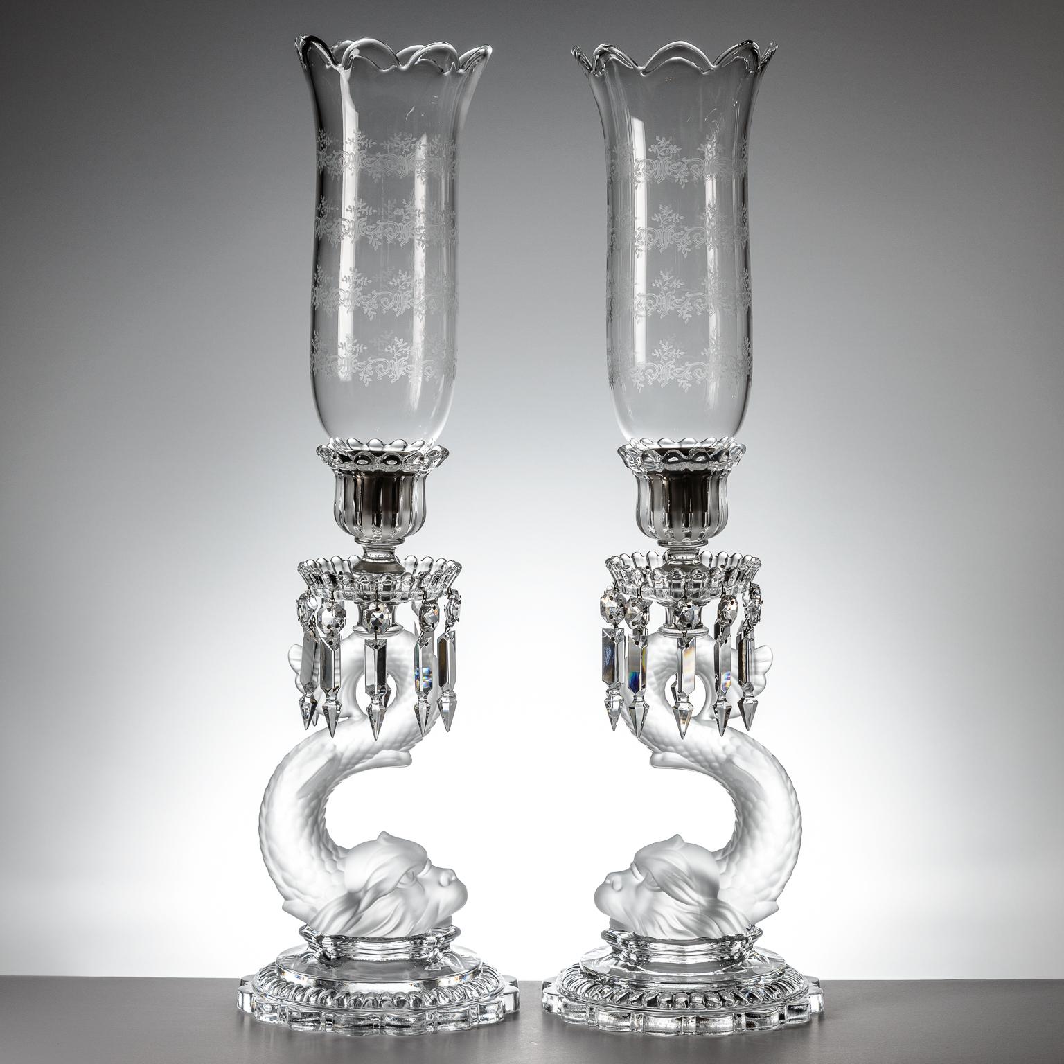A wonderful pair of blown crystal candle sticks featuring Baccarat's classic dolphin base with shaped base, prisms and original tall hurricane globes. This versatile pair can be used with or without their shades for an elegant setting. In very good