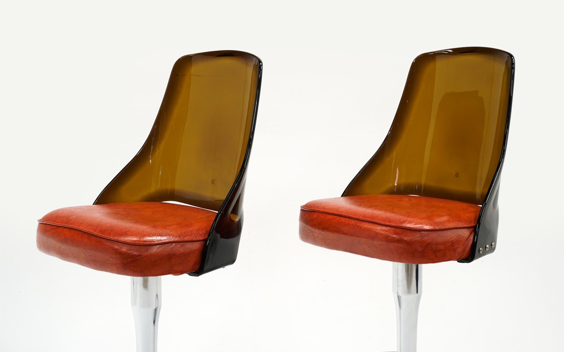Two bar stools with Lucite backs, chrome frames and orange vinyl upholstery. High quality construction with swivel seats. Small tear to the lower portion of one seat that does not detract from the overall appearance. The seats would also be an easy