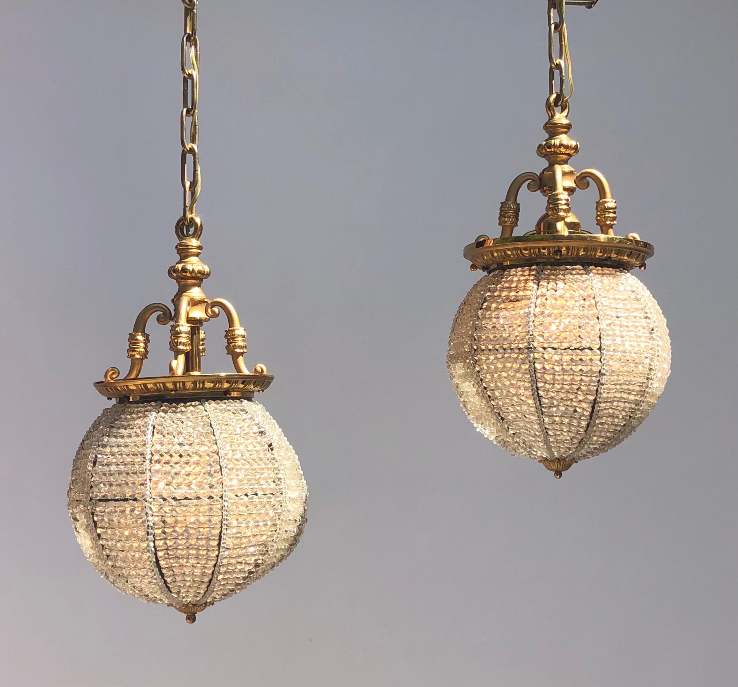 A Magnificent pair of Hand-strung Cut Crystal Sphere Pendants adorned with an elegant matte and high gilt gold finish. This pair of Belle Epoque Cut Crystal Beaded Sphere Chandeliers hang from a Gilt Bronze Egg-and-Dart Ring Console Suspended by