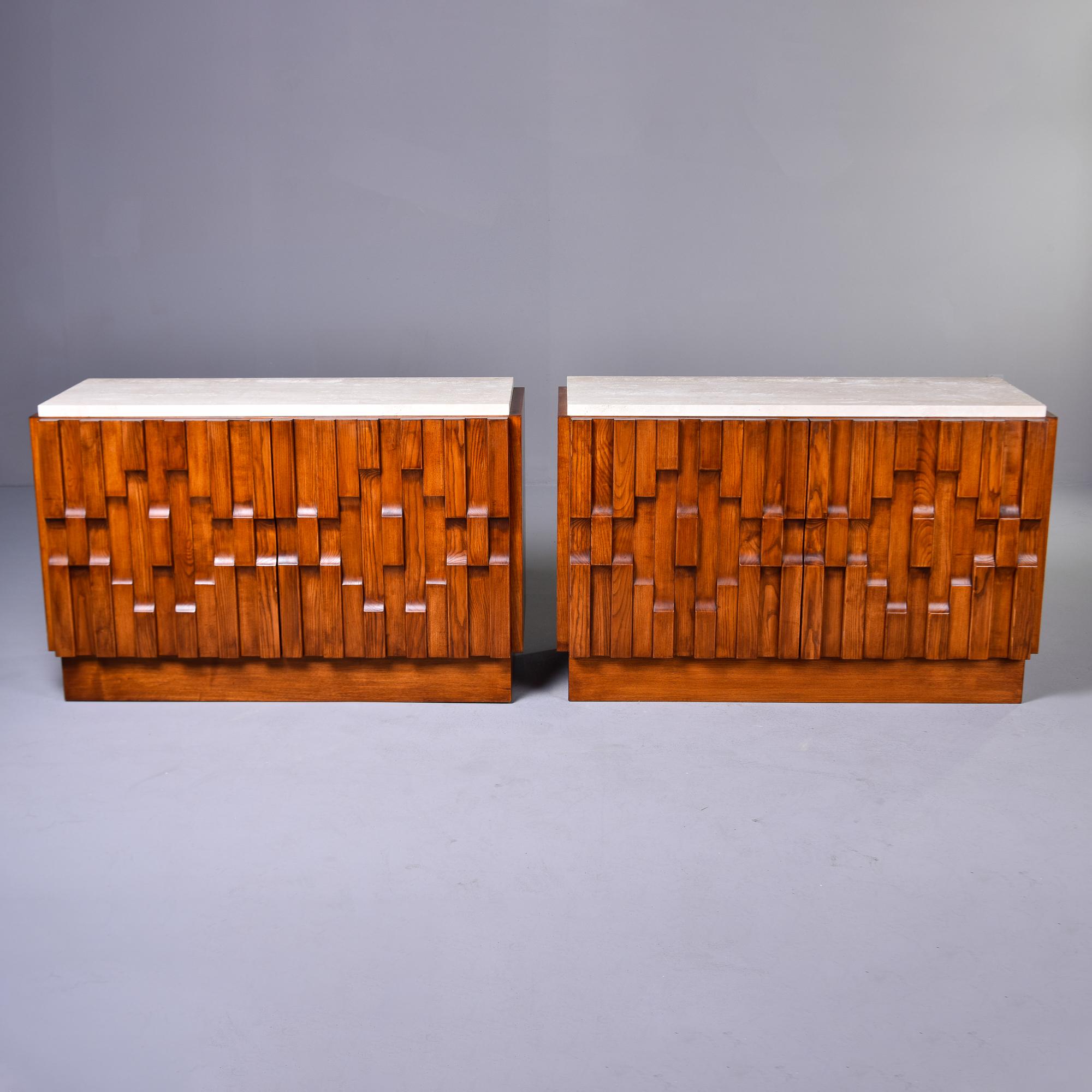 New and custom made for us in England, this pair of cabinets feature travertine tops and sculptural, cubist/brutalist - style fronts. Each cabinet has two hinged doors that open to reveal a storage compartment with a single, adjustable shelf. Each