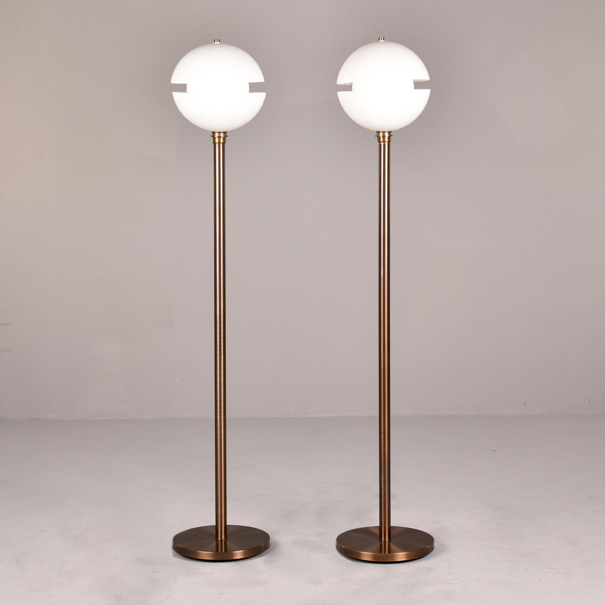 New and custom made by a regional glass artist, this pair of floor lamps have a dark finished brass base and center support with a white glass split globe and inner white globe. This simple yet striking design works well with mid century, modern or