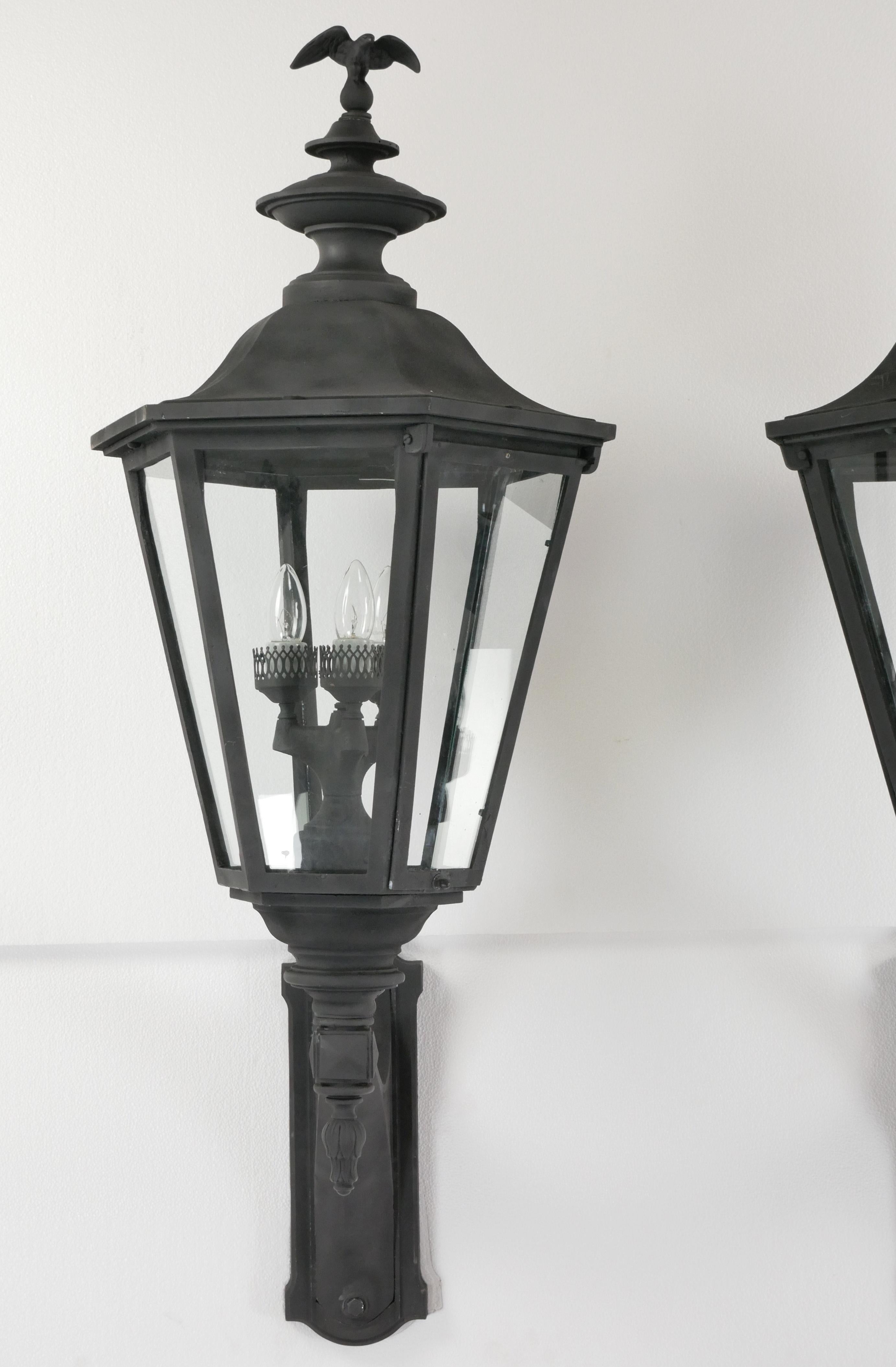 Reclaimed Traditional exterior wall sconces made of black painted aluminum and clear glass panels. Each sconce features an eagle at the very top of the light. Each sconce requires three candelabra light bulbs. The price includes restoration of