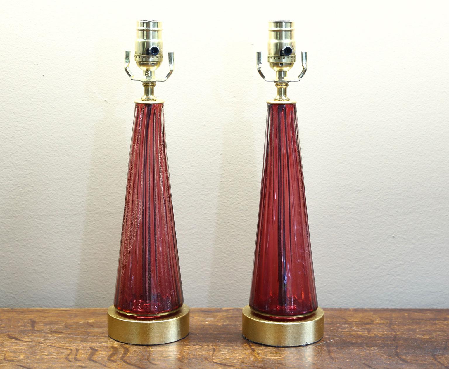 This charming pair of Murano blown glass table lamps has been newly wired for the US using a gold-colored silk cord. The color is a raspberry color with gold flecks. The glass has a pattern of flared reeds. The height is to the top of the socket.