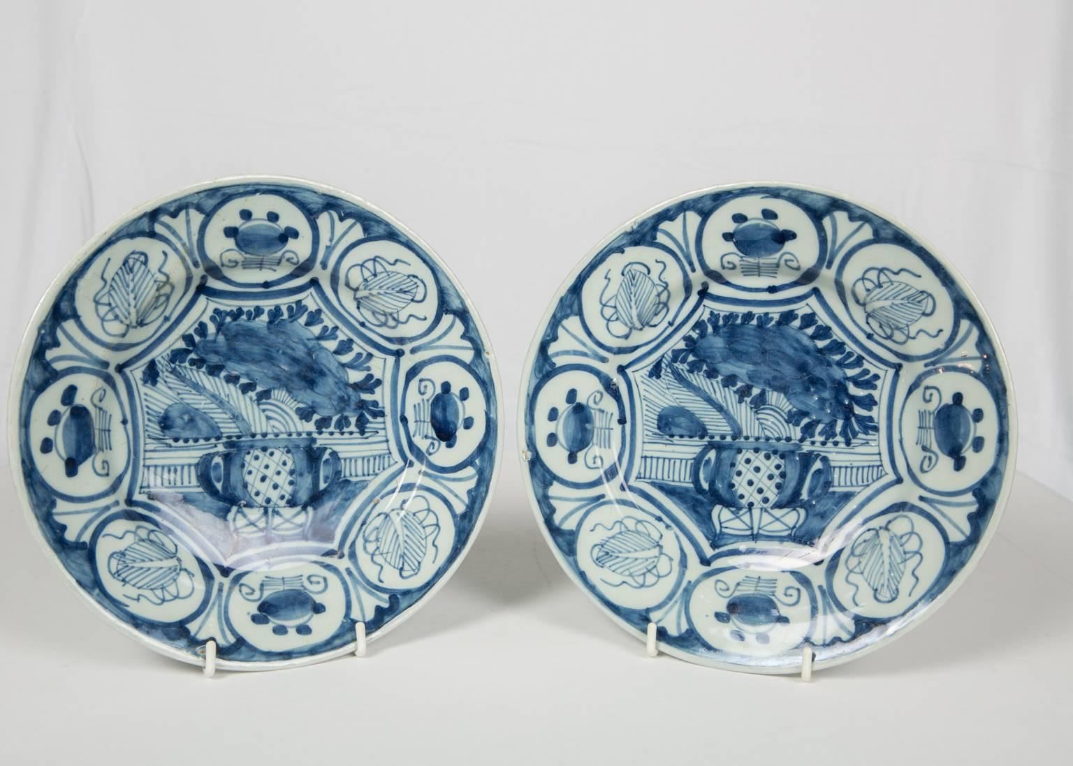 We are pleased to offer this pair of blue and white Dutch Delft dishes with lovely chinoiserie decoration, which features an image of a vase overflowing with flowers. 
Around the vase and flowers is a wide border with symbols of good fortune in the