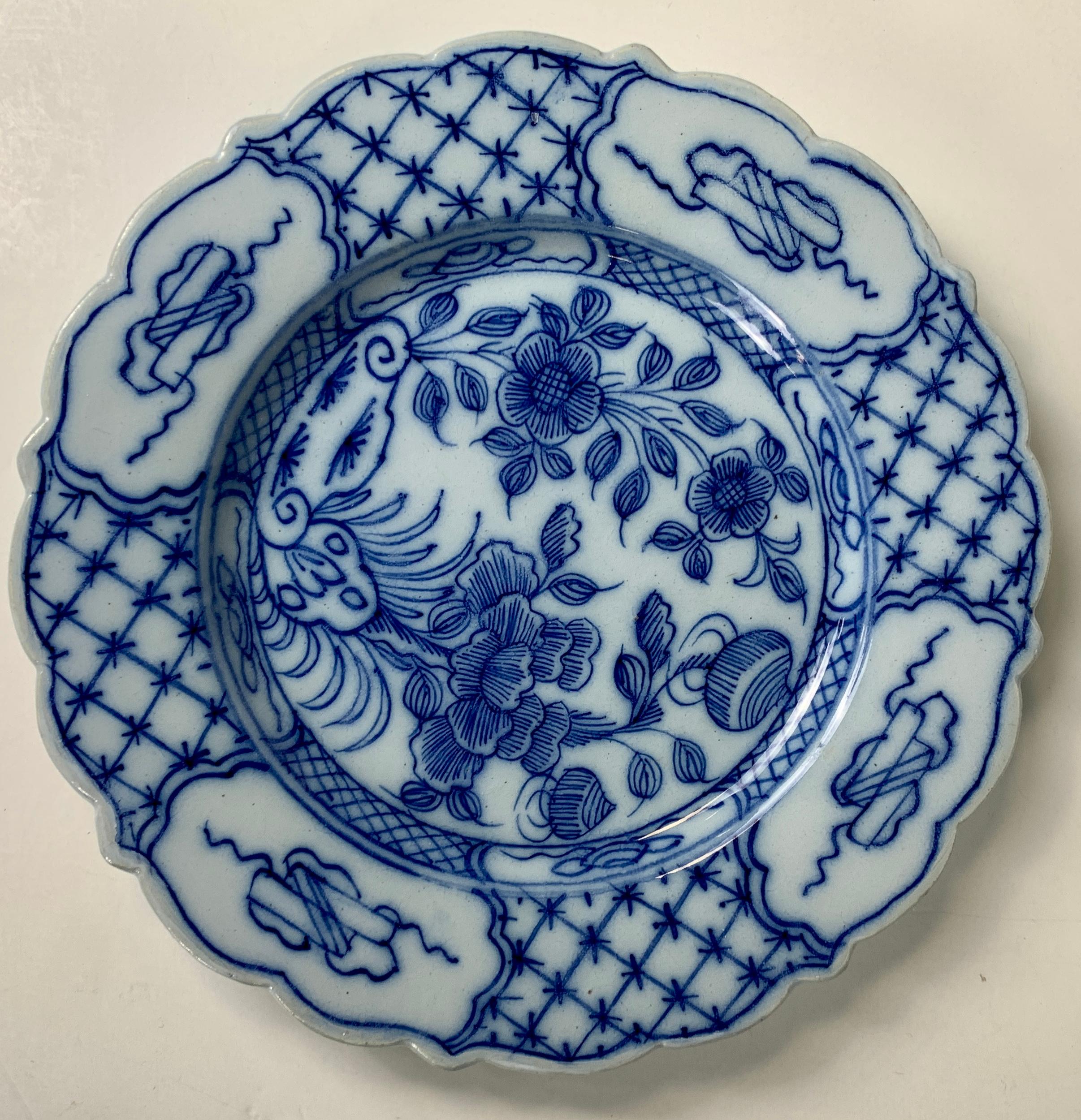 A pair of blue and white Dutch Delft dishes hand-painted in the chinoiserie style. The center of each dish shows two flowering plants in full bloom. Look closely, and you will see that all the painting is done in lines as if by pen or pencil. This