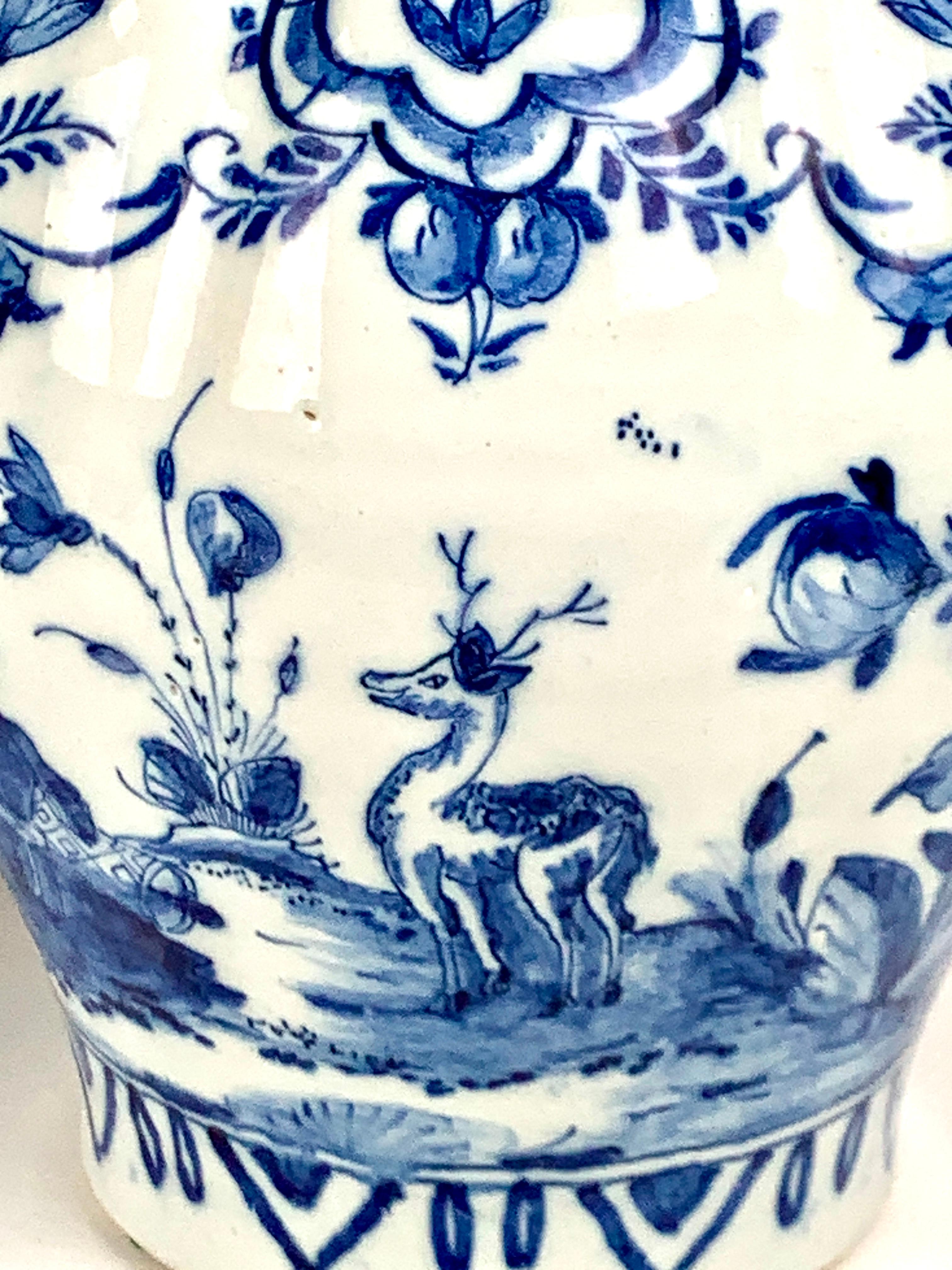 This pair of 18th-century Delft jars has a lovely distinctive style taken from nature.
The cobalt blue designs are hand-painted. 
We see a young woman seated in a garden. 
Budding peonies and a songbird surround her, and a majestic stag evokes a