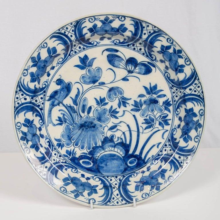 This pair of 18th-century Dutch Delft blue and white chargers were hand-painted. They feature beautiful long-tailed songbirds resting on a flowering branch. 
The garden is lush with exquisite flowers. 
The artist has captured the essence of a garden