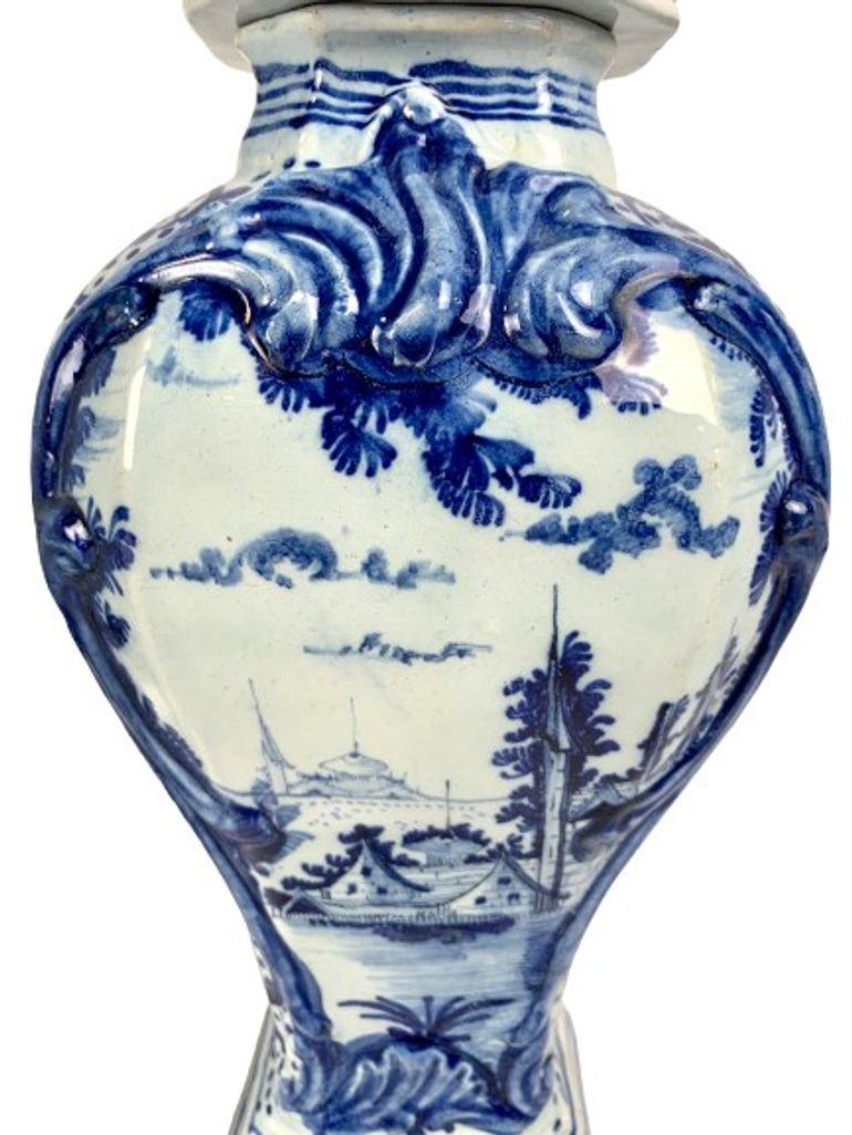 This lovely pair of blue and white Delft mantle jars were hand painted in the Netherlands circa 1780.
We see a chinoiserie scene with a pair of houses waterside in the foreground and a pagoda on the far shore.
The garden scene is framed in a blue