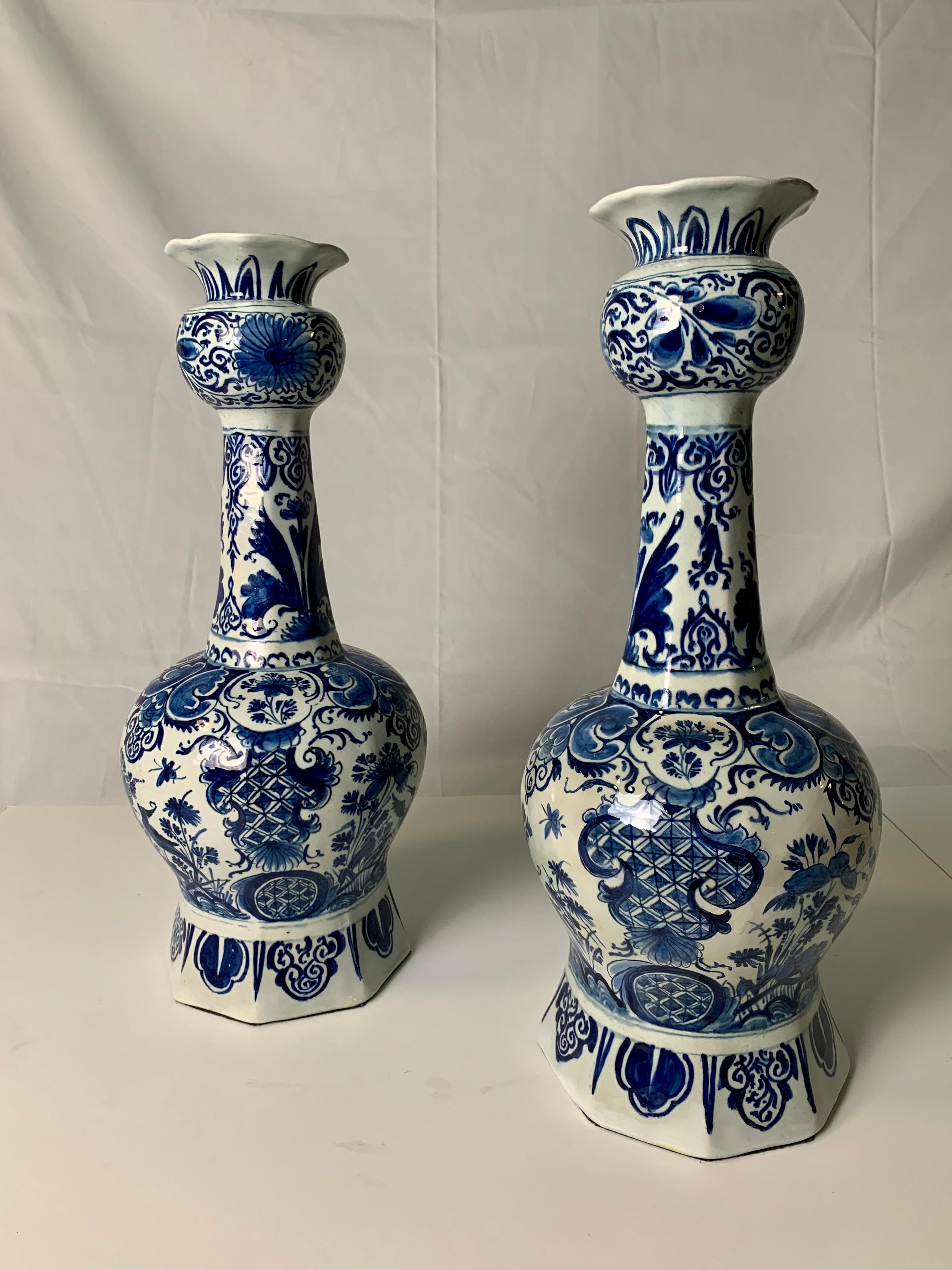 This pair of antique blue and white Dutch Delft vases was made circa 1770. Each vase has four panels with traditional decorations showing garden scenes filled with flowers and songbirds. They have long octagonal necks decorated with scrolling vines