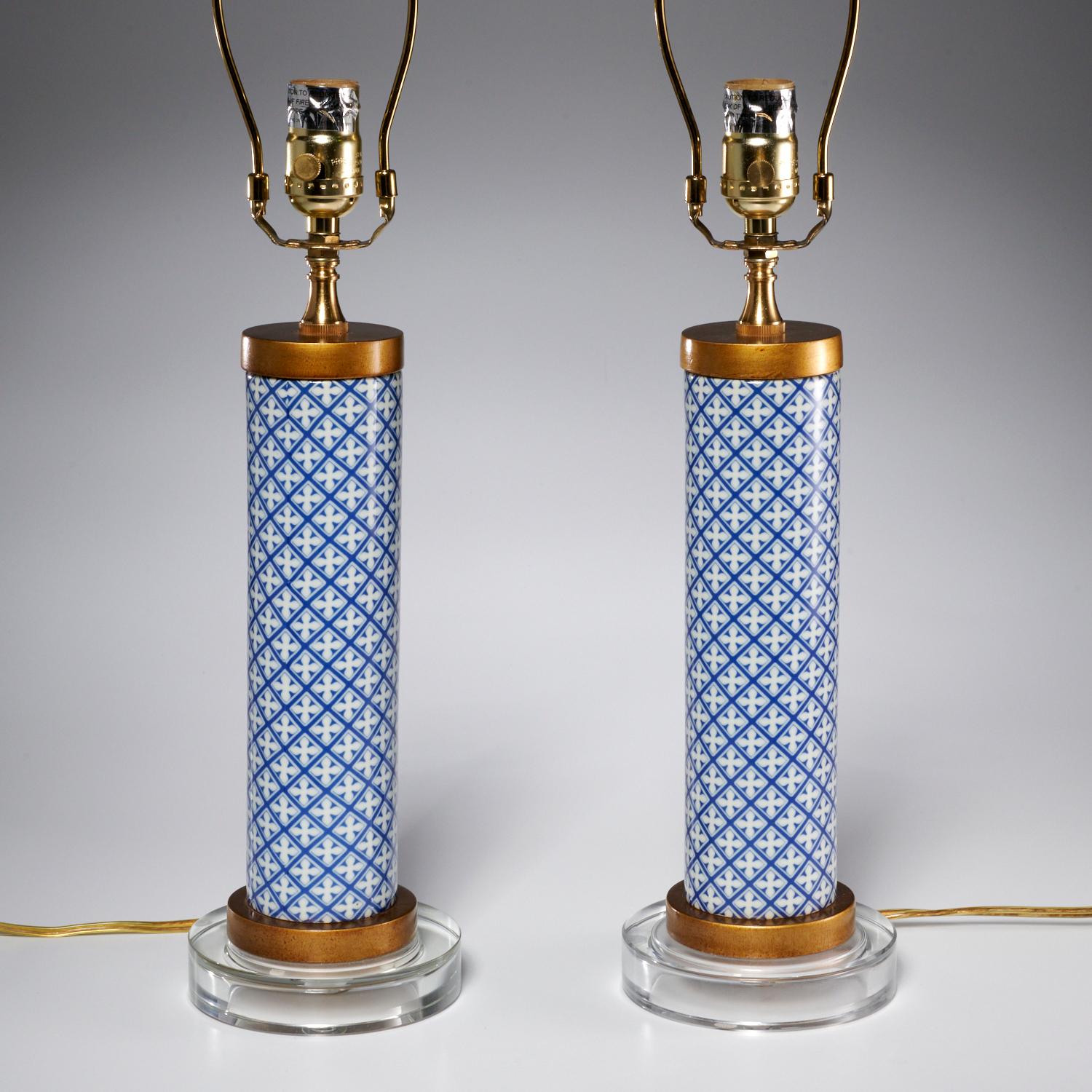 A pair of 21st c., cylinder table lamps in blue and white geometric porcelain with brass and lucite details and pleated white fabric lamp shades. These lamps are very crisp with pleasing clean lines. They come from a beautifully furnished and