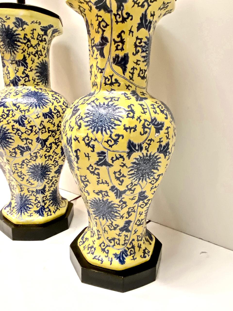 This is an exceptional pair of blue and yellow porcelain chinoiserie table lamps that date to the second half of the 20th century. The 8-sided ceramic bases are fitted with octagonal lacquered wood plinths and double cluster lighting elements. The