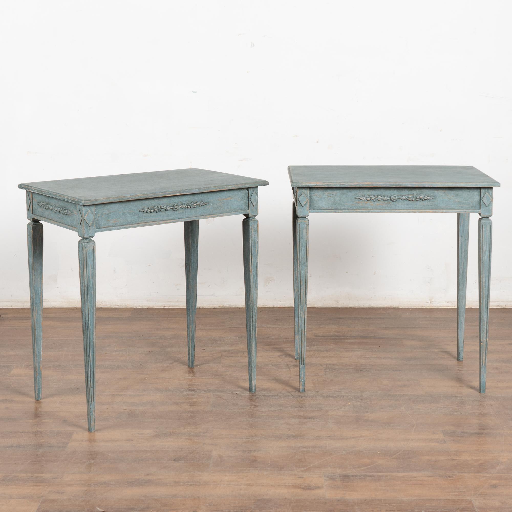 Pair, Gustavian style side tables with slender tapered fluted legs and delicate applied floral carving along skirt. 
Professionally painted in layered shades of blue with mottled white tones, all lightly distressed to fit the1800's era/style that
