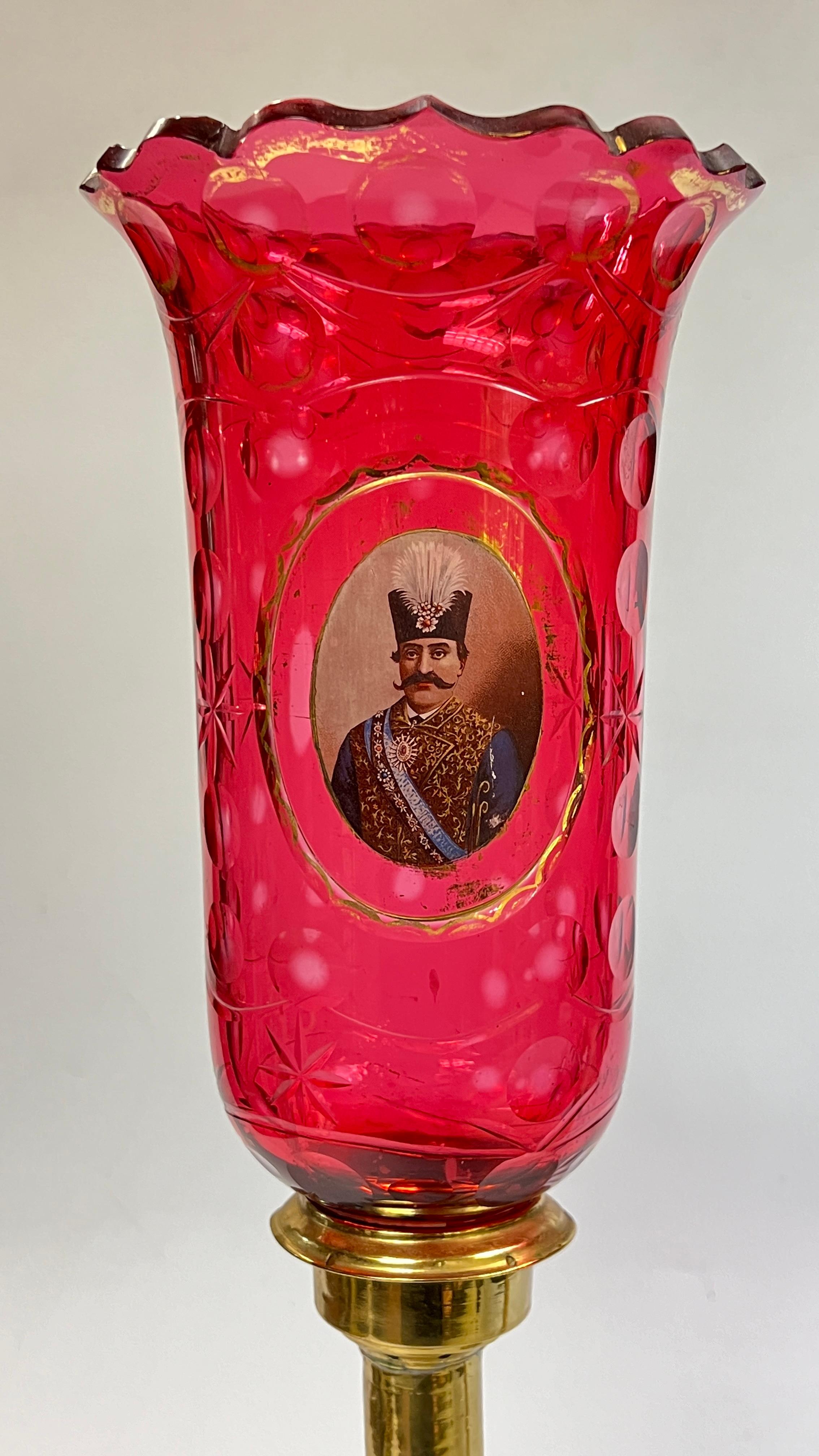 Pair of antique (late 19th century) Russian-made brass candleholders made for the Persian market, with Bohemian ruby red glass hurricane-shaped, cut-glass shades with gilt decorations and the portraits of Naser ad-Din Shah, the fourth and final