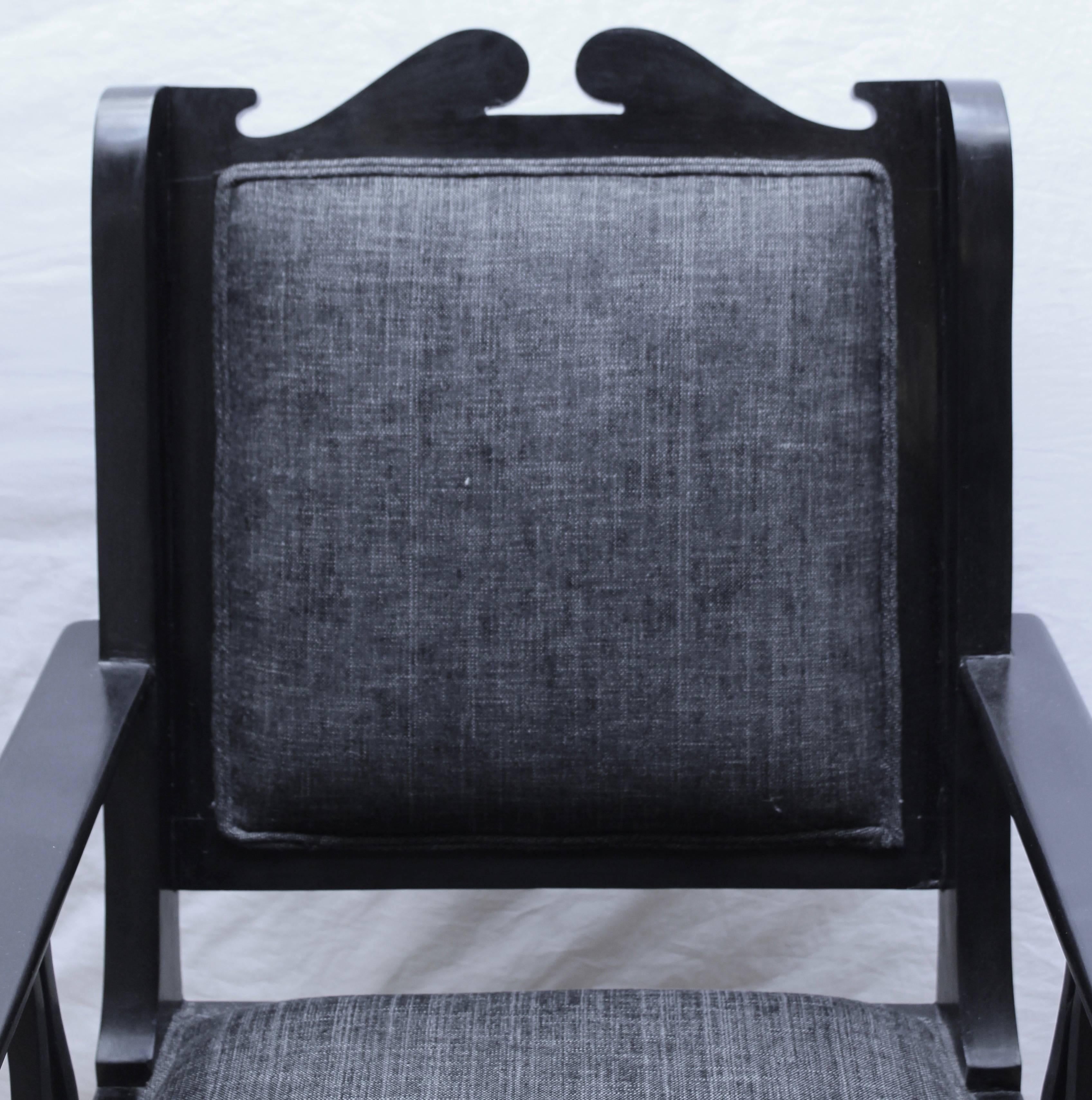 Pair of Indian 20th century Bombay deco ebony armchairs. The heavy frames with simple cut out detailing on the arms legs and 'wings' of the chairs, the top with a broken pediment. Upholstered in later charcoal upholstery.
 