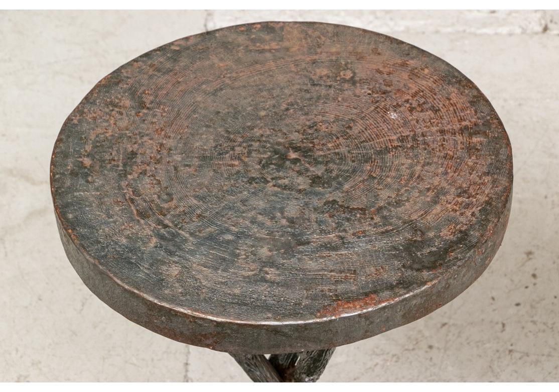 A rarely seen pair of organic branch form end tables for use inside or out. With circular tops with concentric thin circles in bands. Mounted on textured and naturalistic branch form tripod bases. In a great old worn patina overall with some