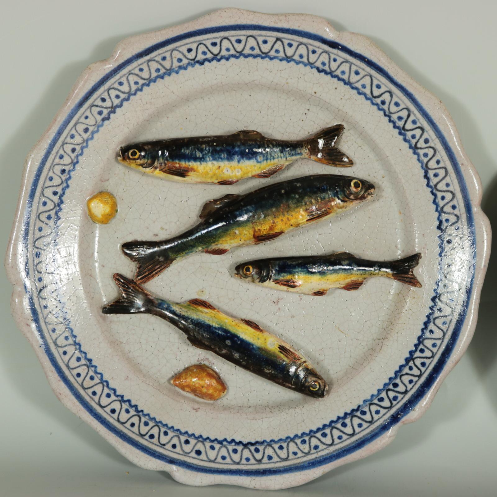 Paire d'assiettes Brard en majolique française de Palissy, représentant des poissons et des coquillages disposés sur un fond blanc. L'une des assiettes présente également une langoustine, ce qui est inhabituel. Bordures géométriques peintes à la