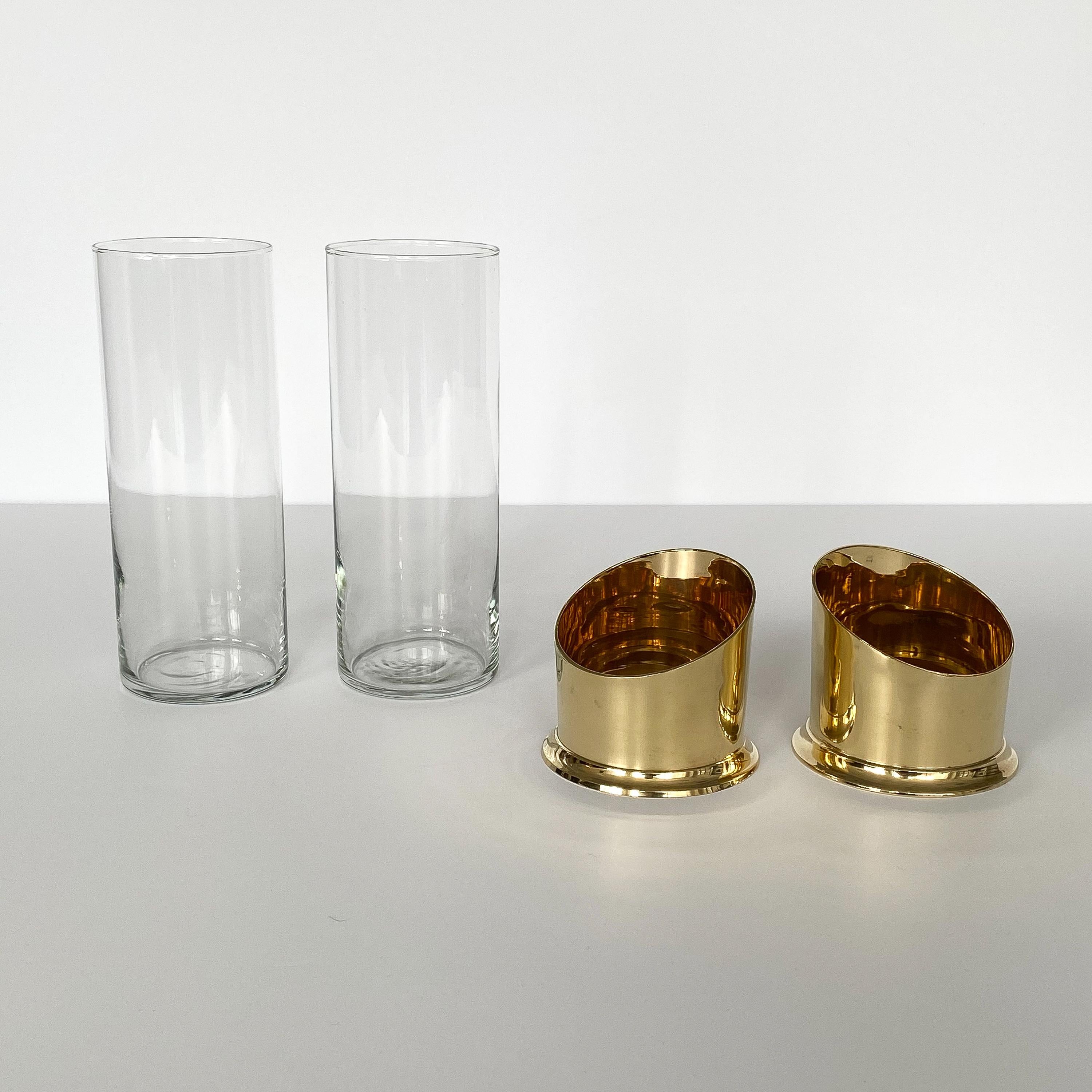 Pair of brass and glass hurricane candleholders or vases. Solid unlacquered brass bases with bias cut asymmetrical design. Bases hold glass hurricanes / vases. Glass is removable from base for easy cleaning. Glass opening 3.25