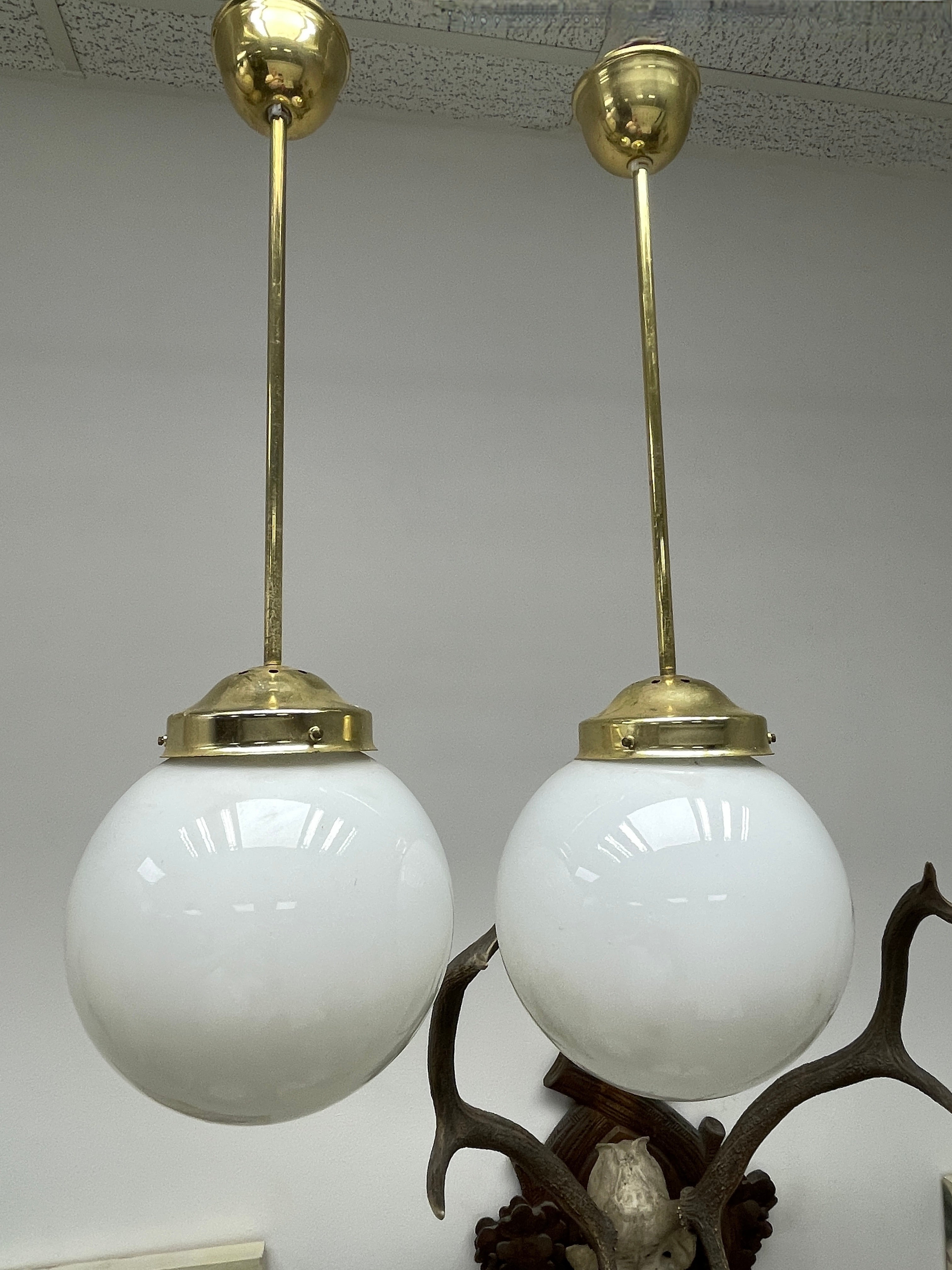Add a touch of opulence to your home with this charming set of two chandeliers or light pendants! Perfect brass fixtures hold a big milk glass globe, to enhance any chic or eclectic home. We'd love to see it hanging in an entryway as a charming