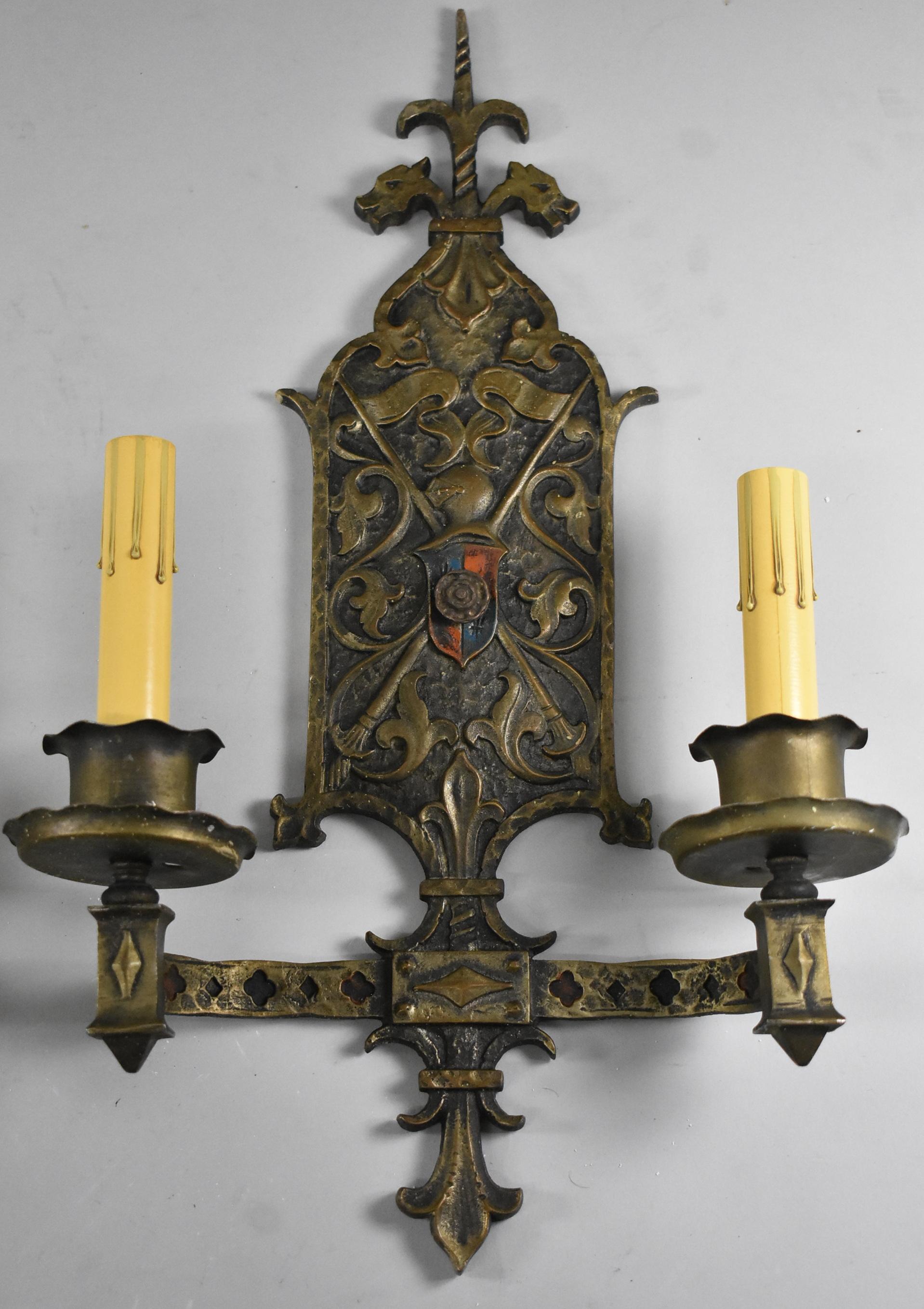 Pair of brass Gothic Revival two candelabra socket wall sconces. Original finish with aged brass patina, circa 1920s. Two dragon heads flank the top with knight and center shield.
