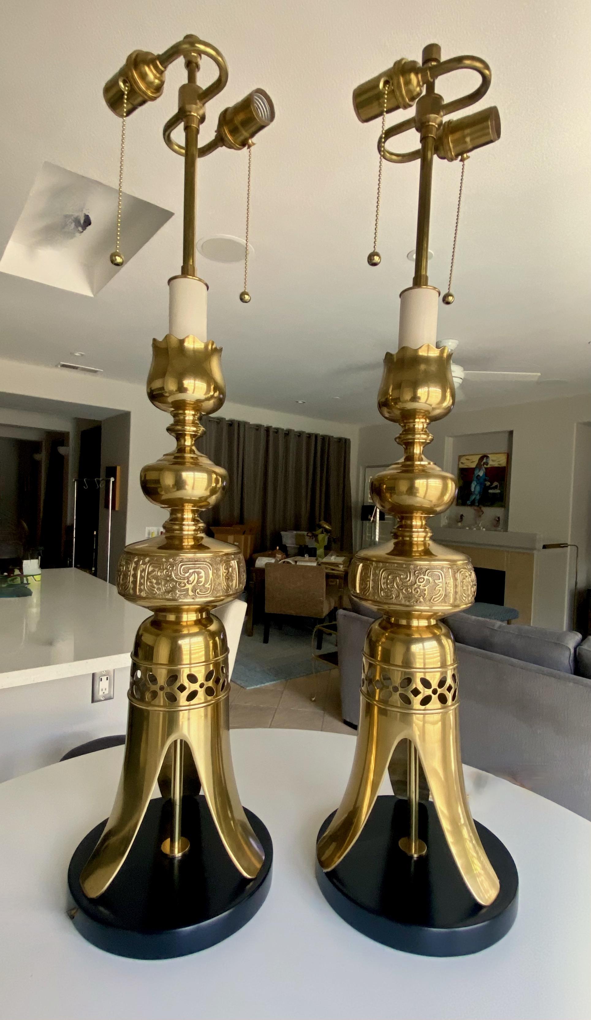 Pair solid brass James Mont Asian style candle sticks converted to table lamps resting on black lacquered wood bases. Newly wired with new French style rayon covered cords and new brass double cluster fittings. The condition of the brass finish and