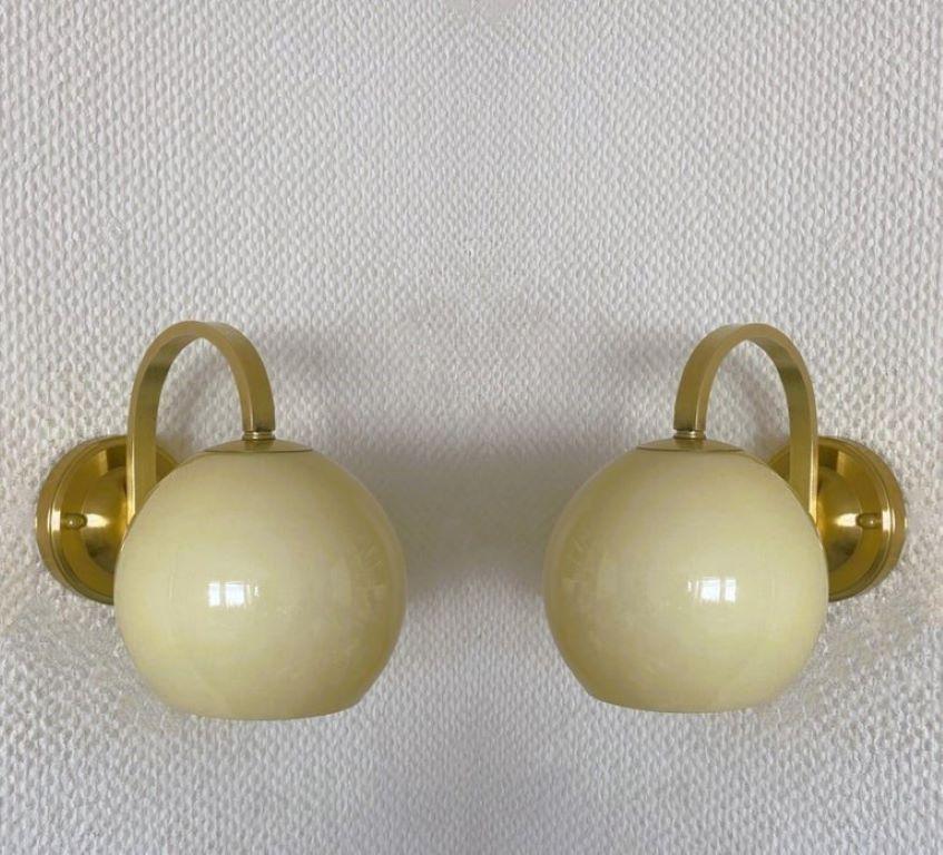 A pair of brass and glass wall lights attributed to Paavo Tynell, Finland, 1950s. Clean lines design from the Scandinavian Modern period, opaline glass shades in cream color. In good vintage condition, no damages, brass with some wear and aging