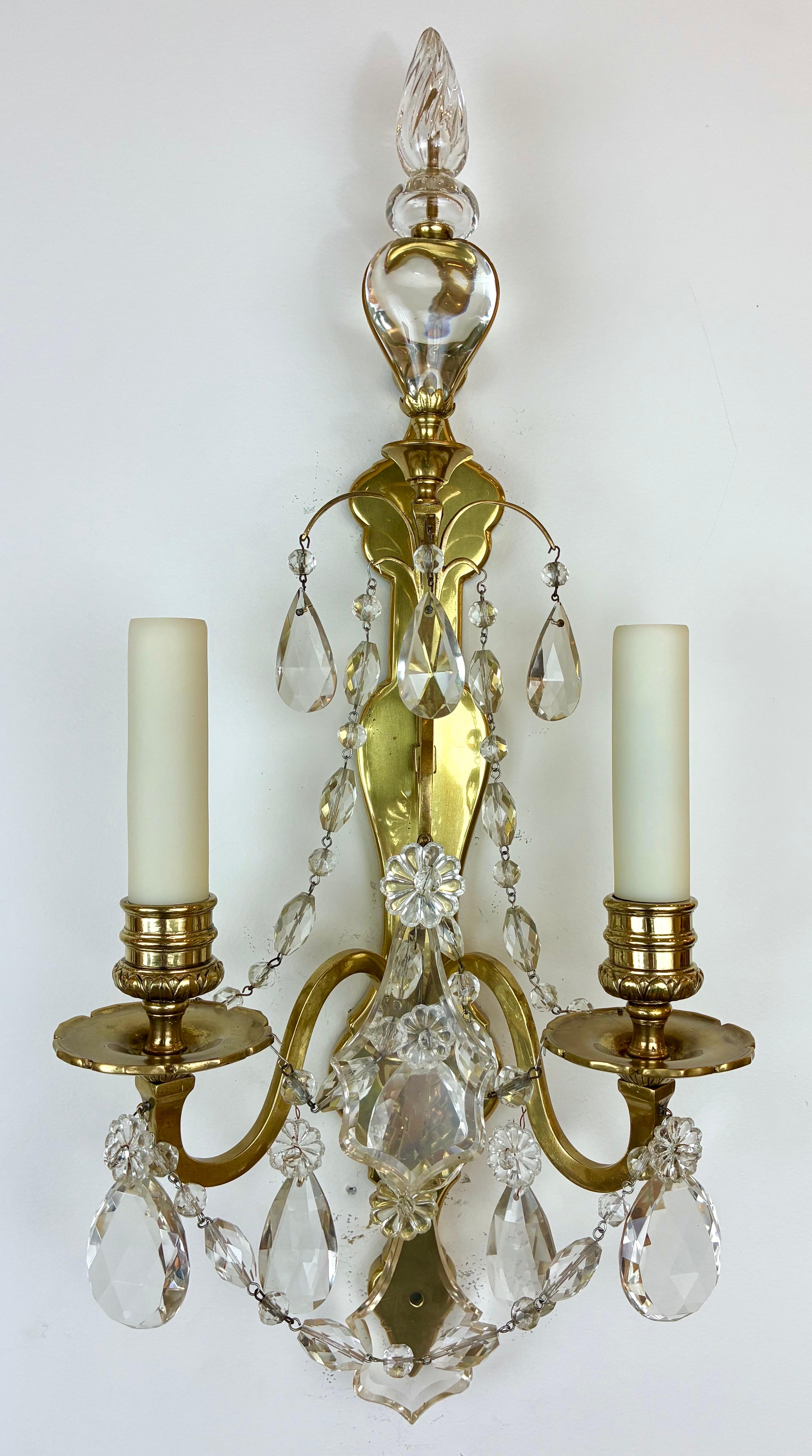 Questa coppia di due appliques di prima qualità è opera del rinomato designer E F. A. Caldwell e si trova negli archivi Caldwell dello Smithsonian.
Presentano una catena di perline sfaccettate, gocce di cristallo tagliate a mano e sono sormontate da