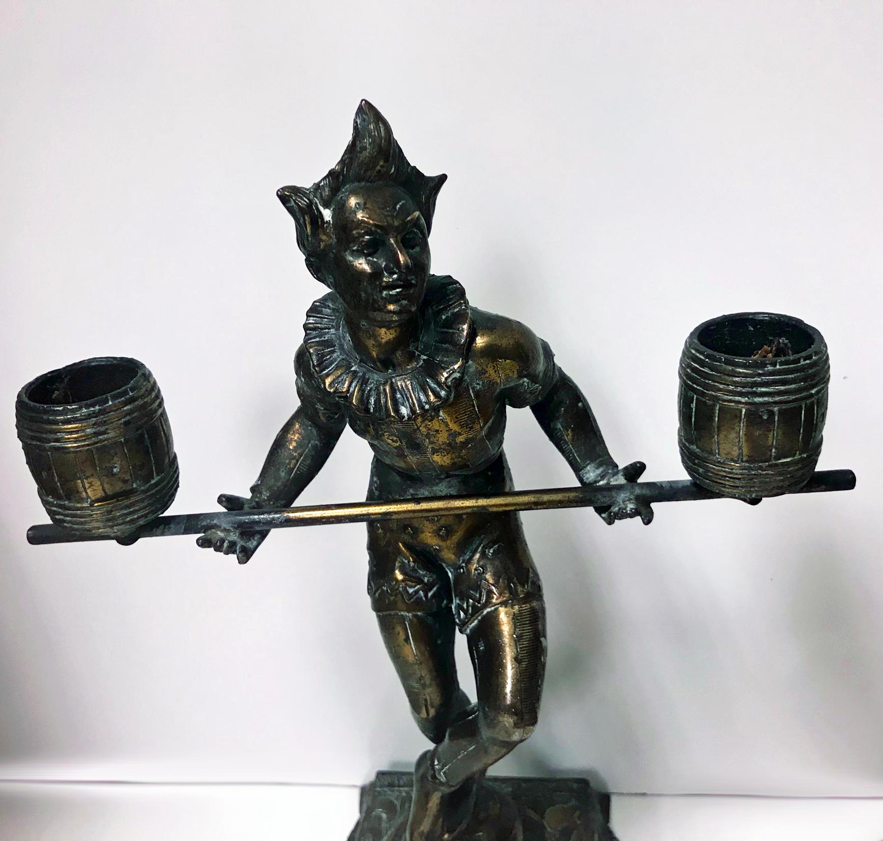 Pair of bronze clown candlesticks sculptures, probably French, circa 1890. Each depicting a clown in costume balancing two barrels on a pole forming candleholders with one leg balancing on a ball. All surmounted on eastern carpet style base