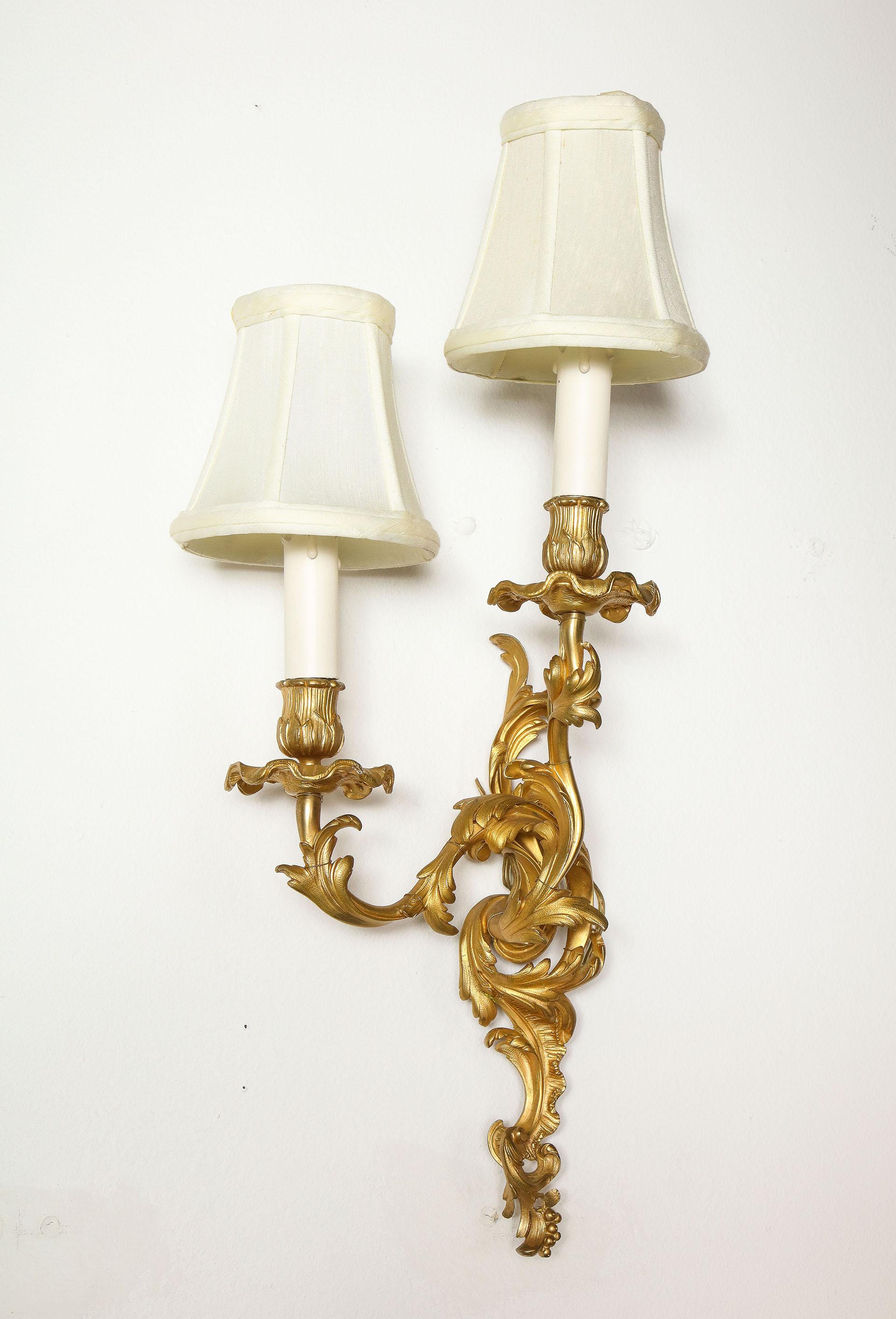 Probably Napoleon III in the Louis XV style, the chased bronze wall lights each with a scroll work back plate supporting a staggered pair of similarly scrolled arms.
