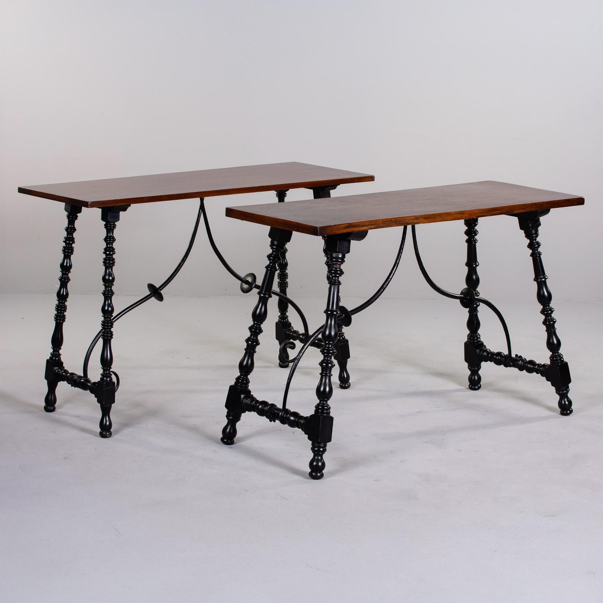 Found in England, this pair of console tables date from approximately 1900. Rectangular mahogany tops are just under 48” wide and are supported with contrasting very dark stained and turned legs with decorative iron stretchers. Unknown maker. Sold