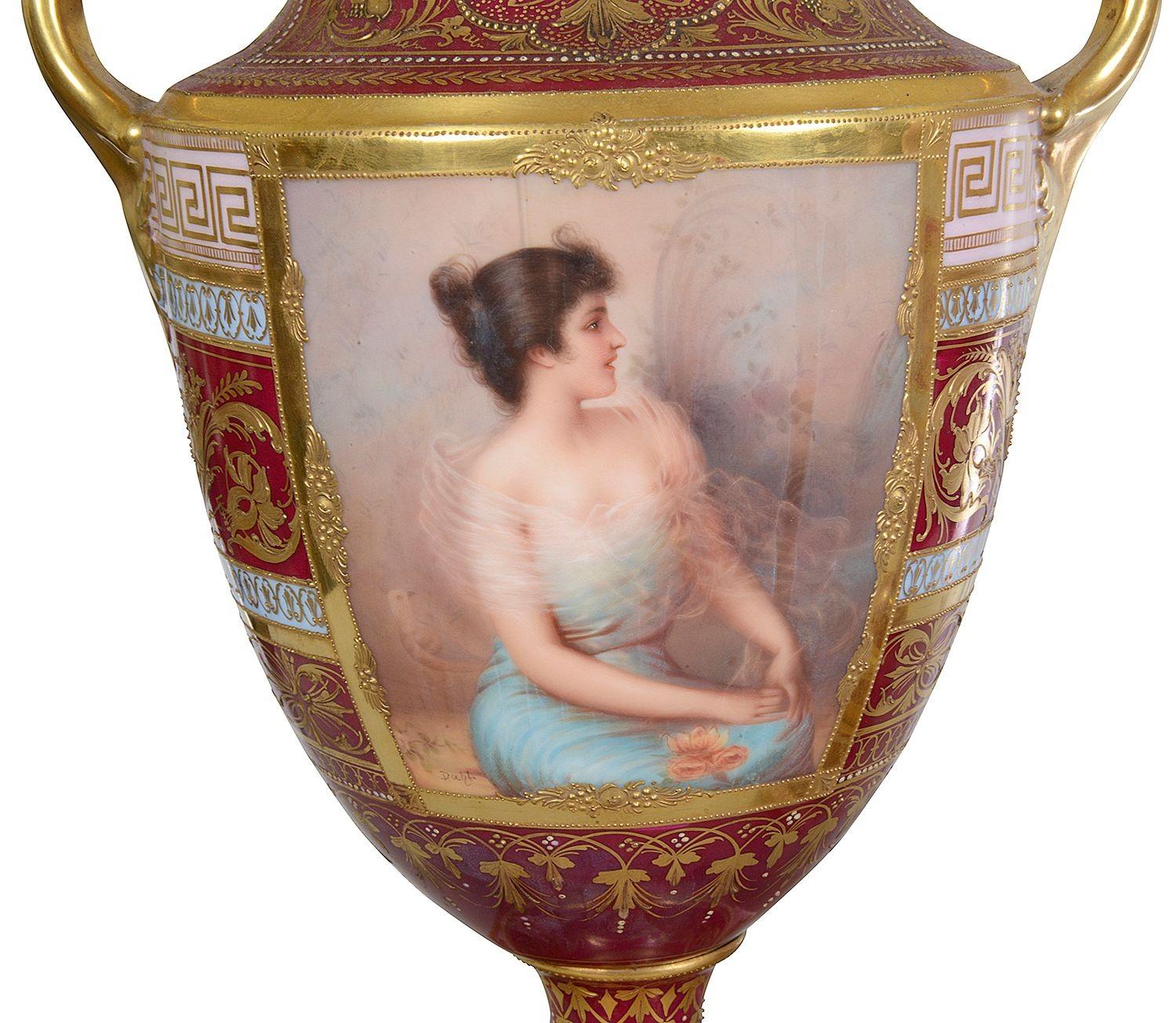 This pair of late 19th-century Vienna porcelain lidded urns showcases exquisite craftsmanship and elegance. Each urn features a striking form with a domed lid and ornate handles, reflecting the stylish design of the era. The vibrant red and gold